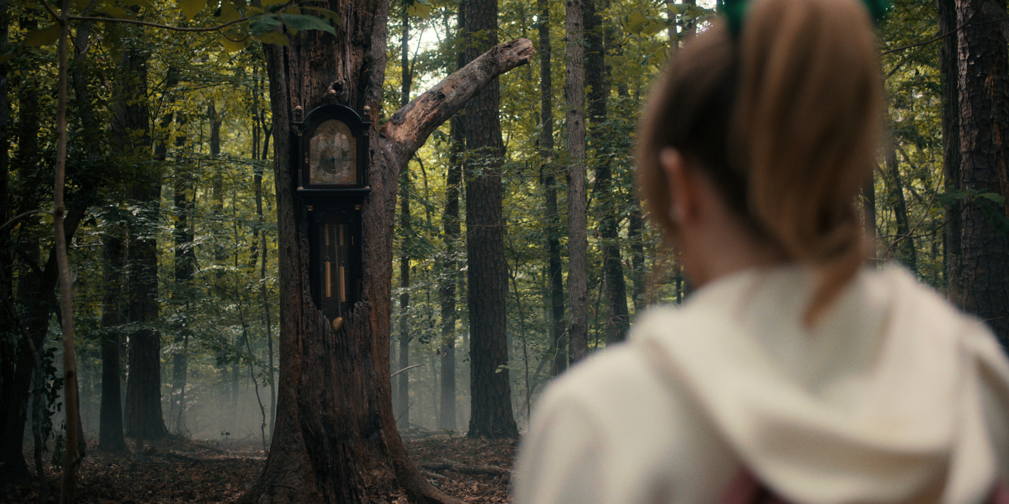 Une jeune femme regarde fixement une horloge grand-père encastrée dans un tronc d'arbre.