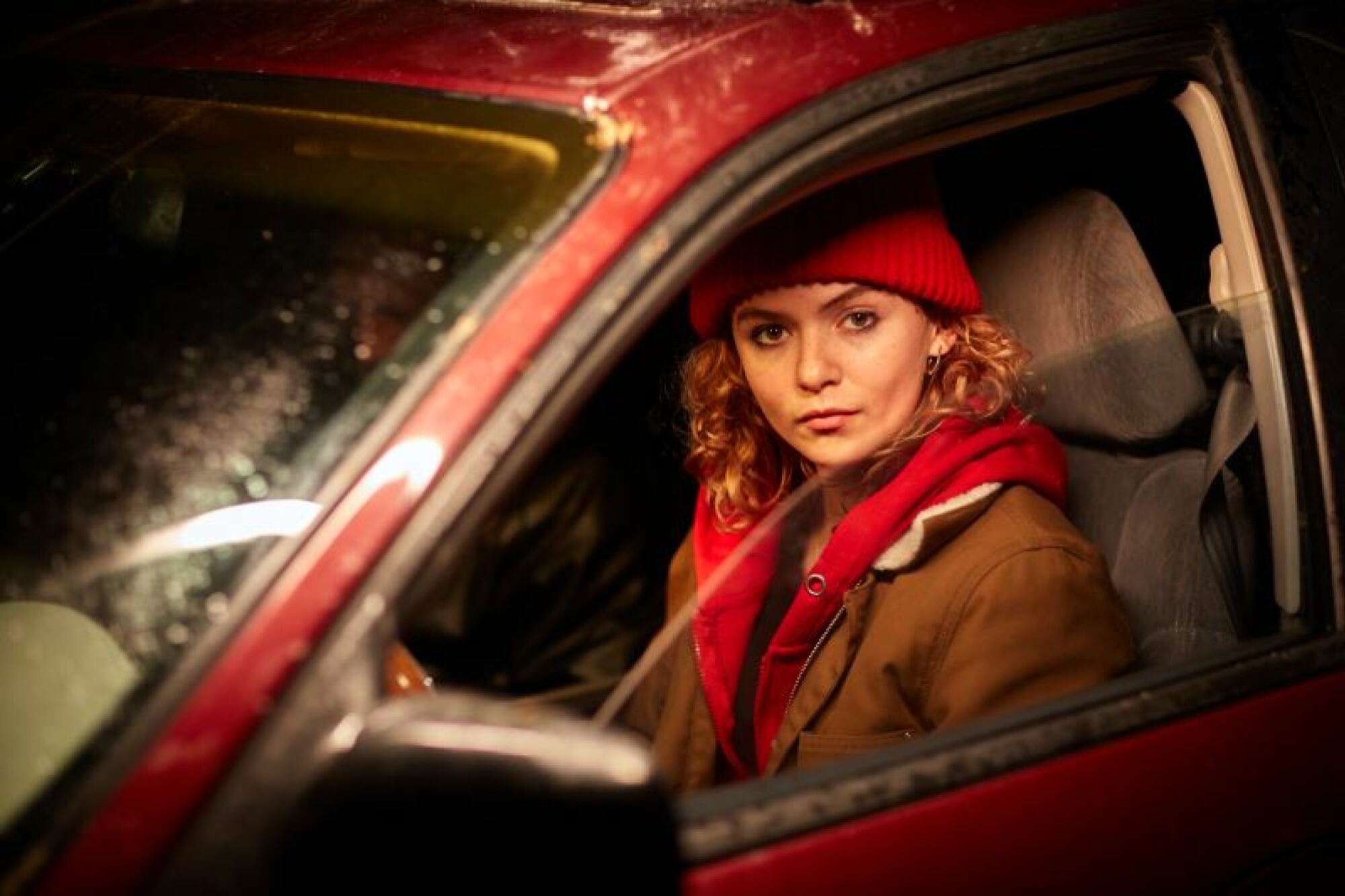 Une femme au chapeau rouge est assise dans une voiture rouge.