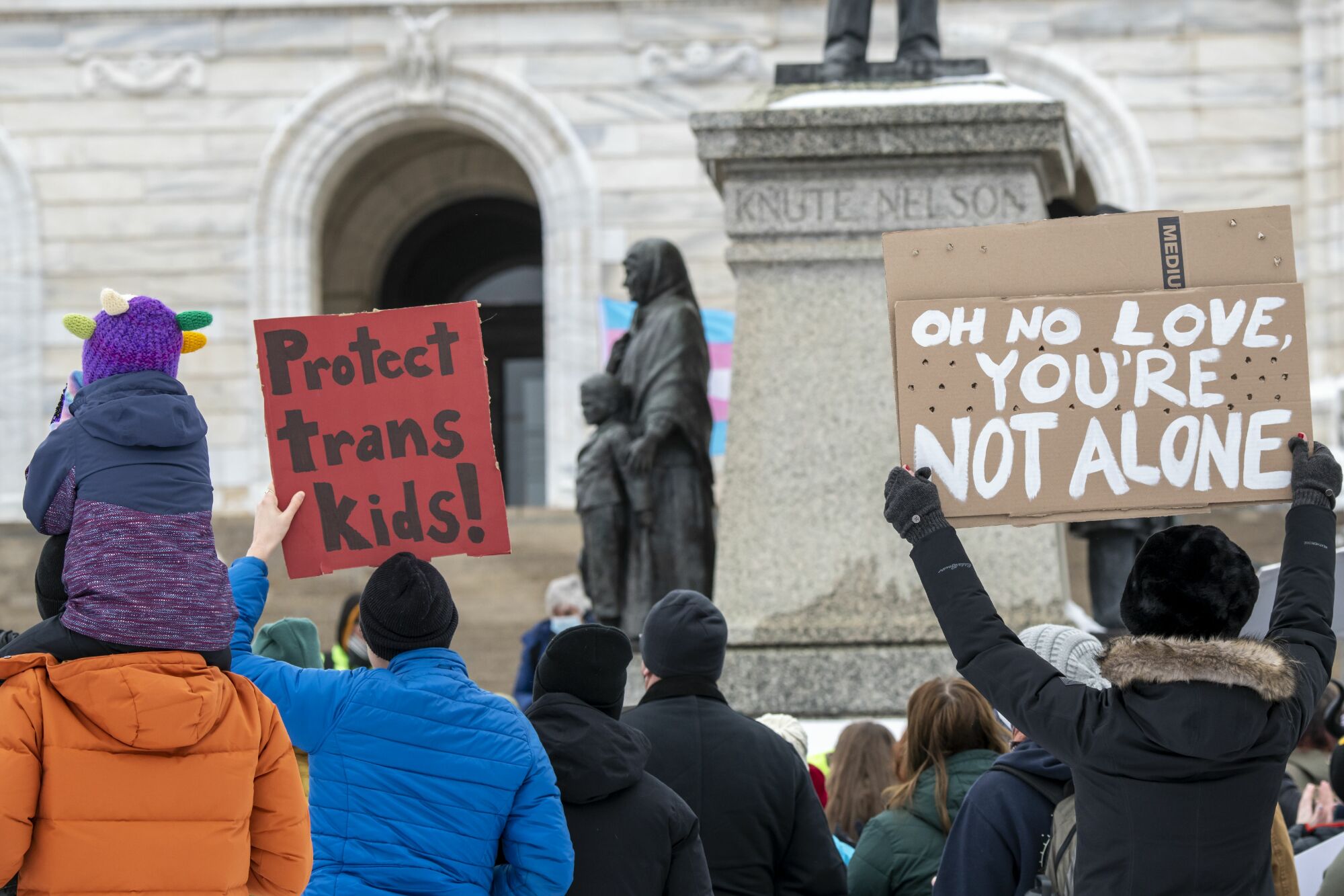 Une photo de manifestants tenant des pancartes lisant "Protéger les enfants trans" et "Tu n'es pas seul".