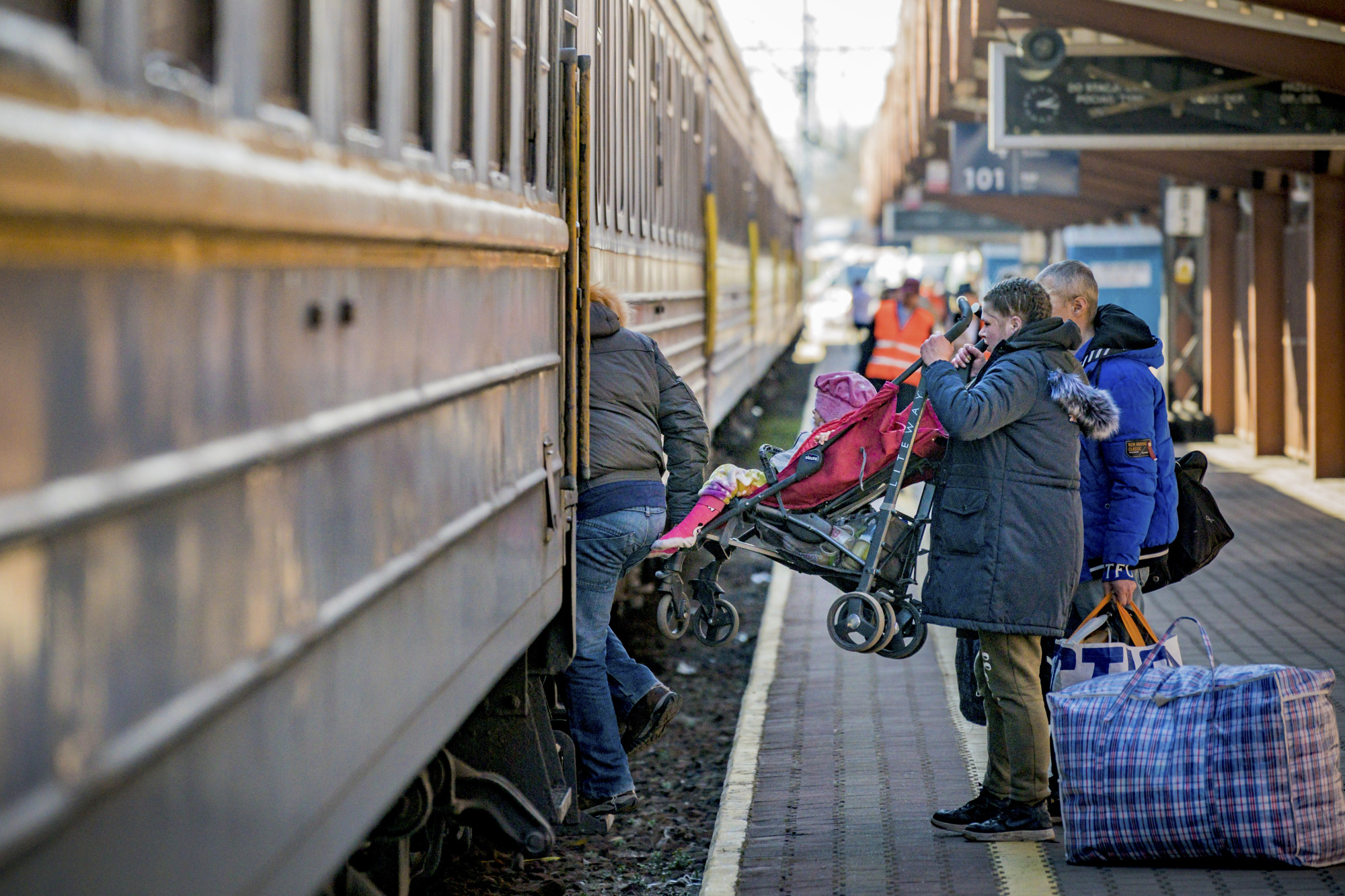 Deux personnes retirent une poussette avec un enfant à l'intérieur d'un train de voyageurs.