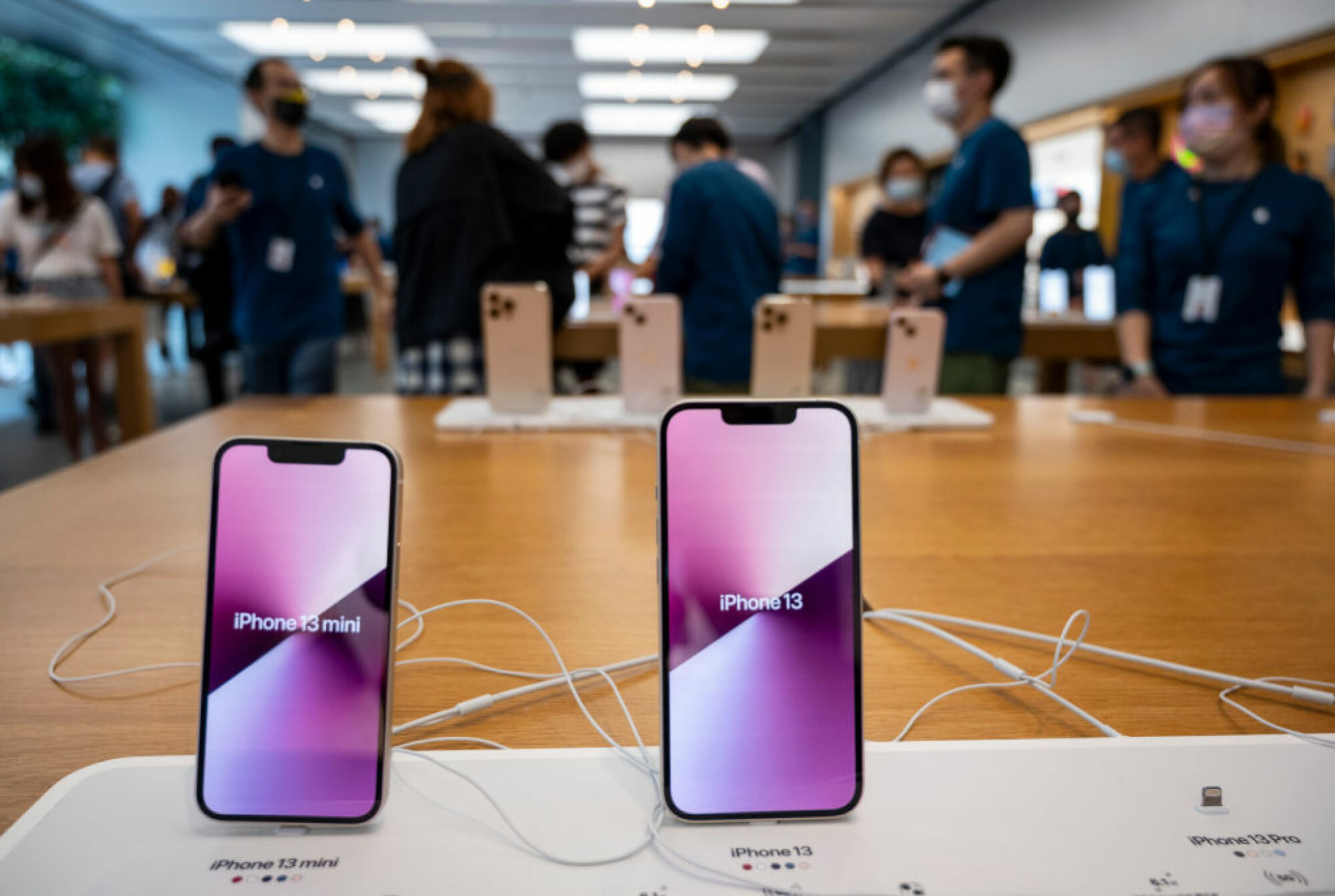 Deux iPhones à l'Apple Store avec leurs noms à l'écran.  iPhone 13 mini à gauche, iPhone 13 à droite.