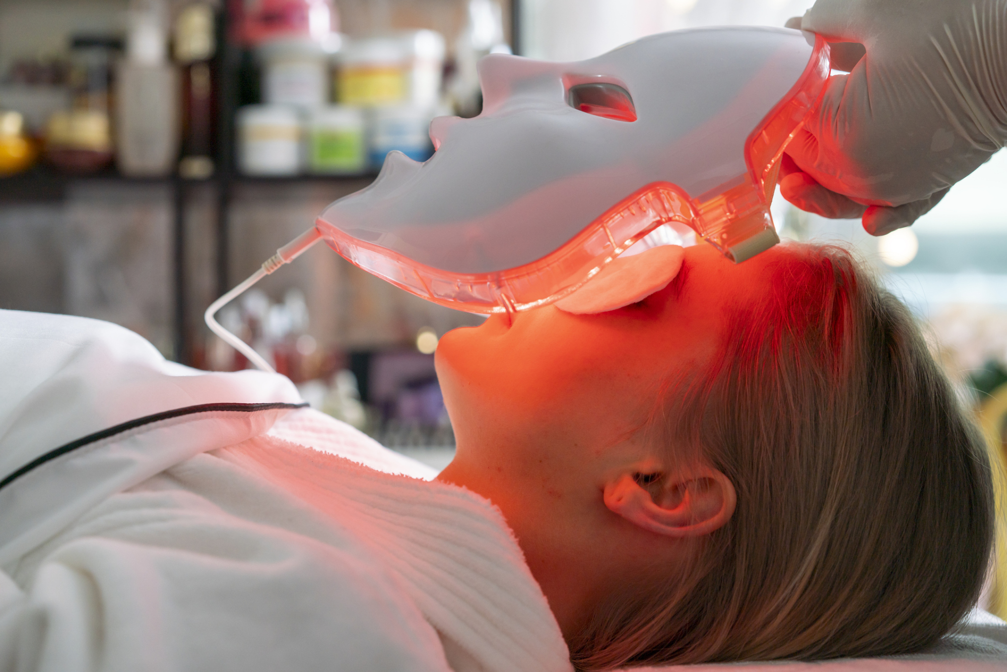 Femme allongée avec une protection oculaire, un masque facial blanc avec des lumières rougeoyantes est abaissé sur son visage.