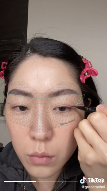 Une femme asiatique aux cheveux noirs regarde la caméra et applique un eye-liner avec un filtre superposé.