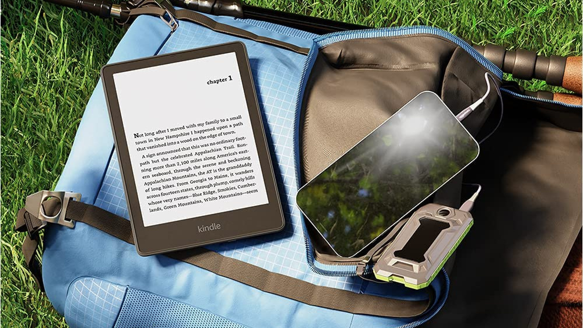 Tablette Kindle noire affichant une demi-page de texte, la tablette se trouve à côté d'un iPhone sur une couverture bleue au-dessus de l'herbe verte. 