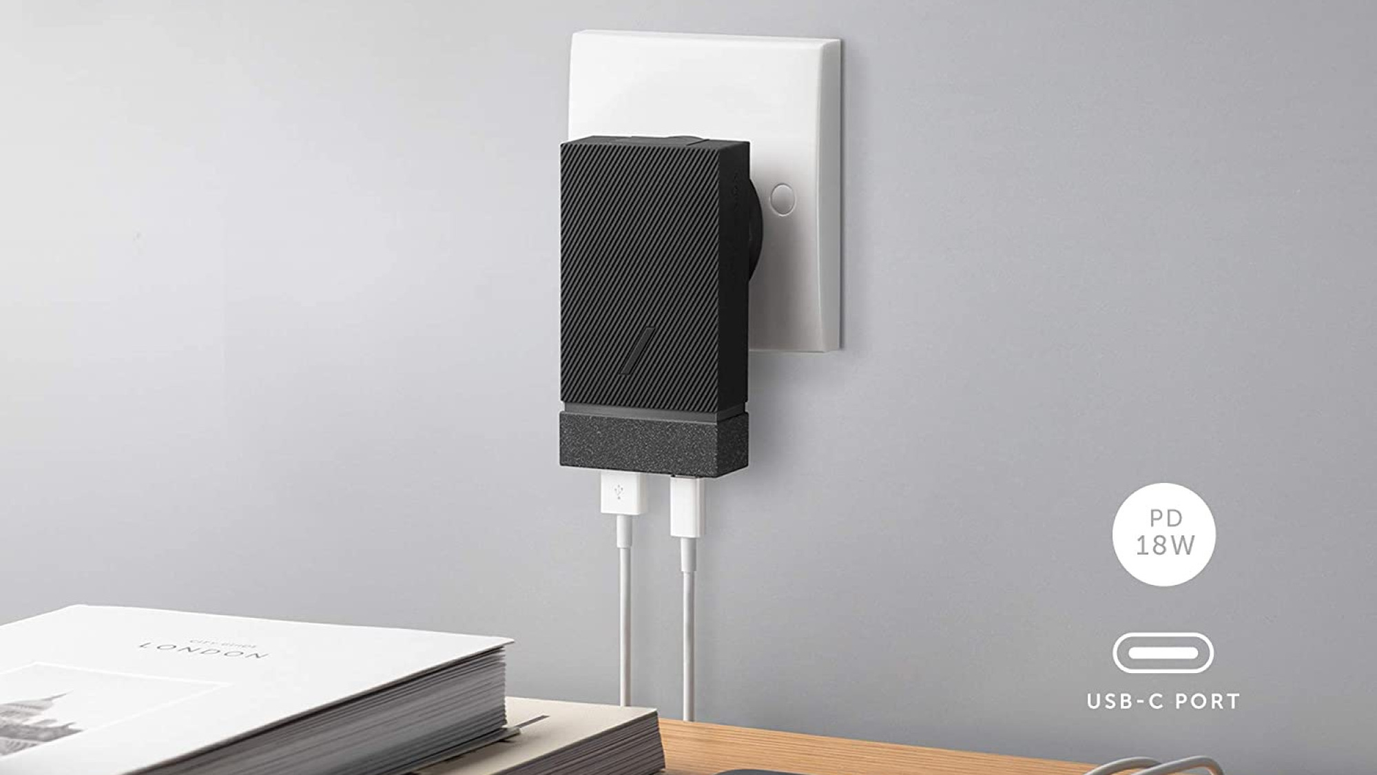 Adaptateur noir en forme de rectangle branché au mur, avec deux cordons blancs branchés au bas de celui-ci.