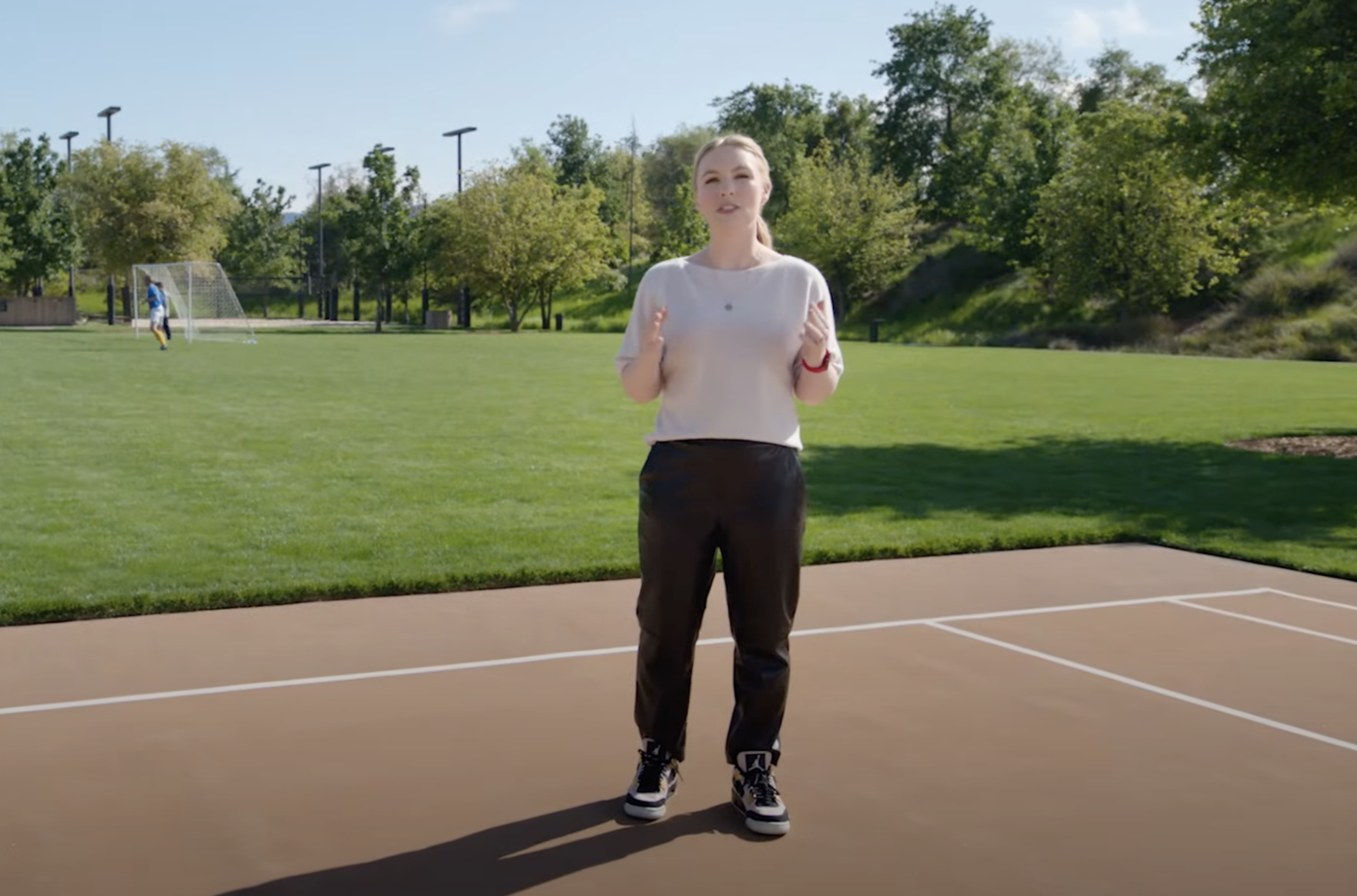 Rubie Edmondson porte un t-shirt blanc, un pantalon noir en cuir, une montre Apple rouge et des Air Jordan montantes noires et blanches.