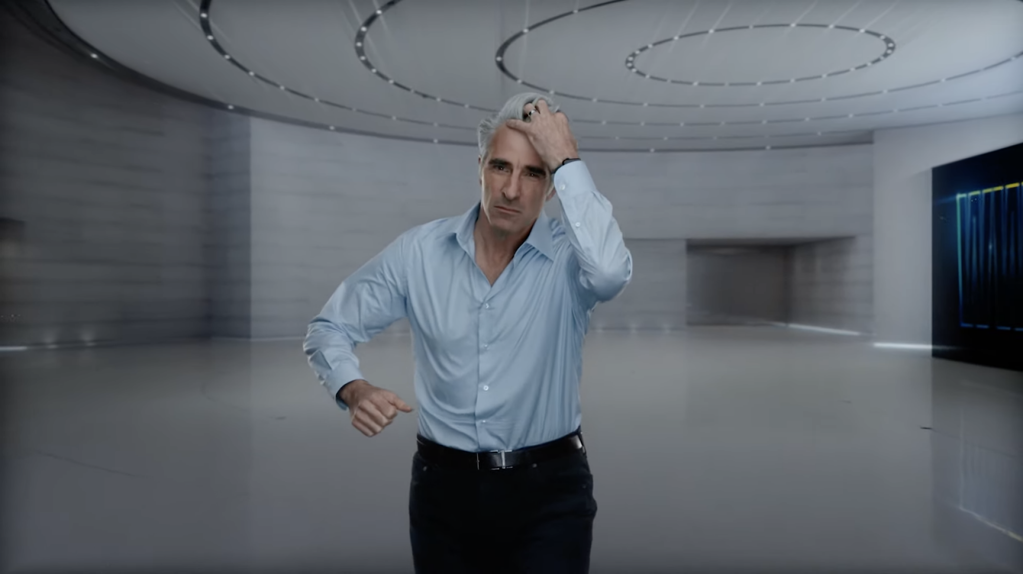 Craig Federighi passe une main dans ses cheveux gris.  il porte une chemise bleue et un pantalon noir.