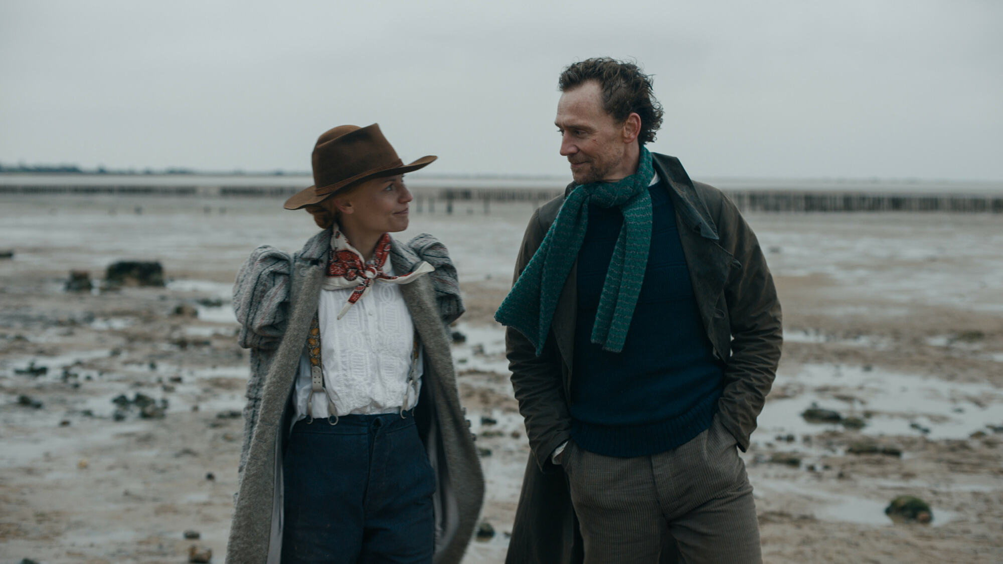 Une femme et un homme portant des vêtements chauds à l'ancienne sur une plage grise.