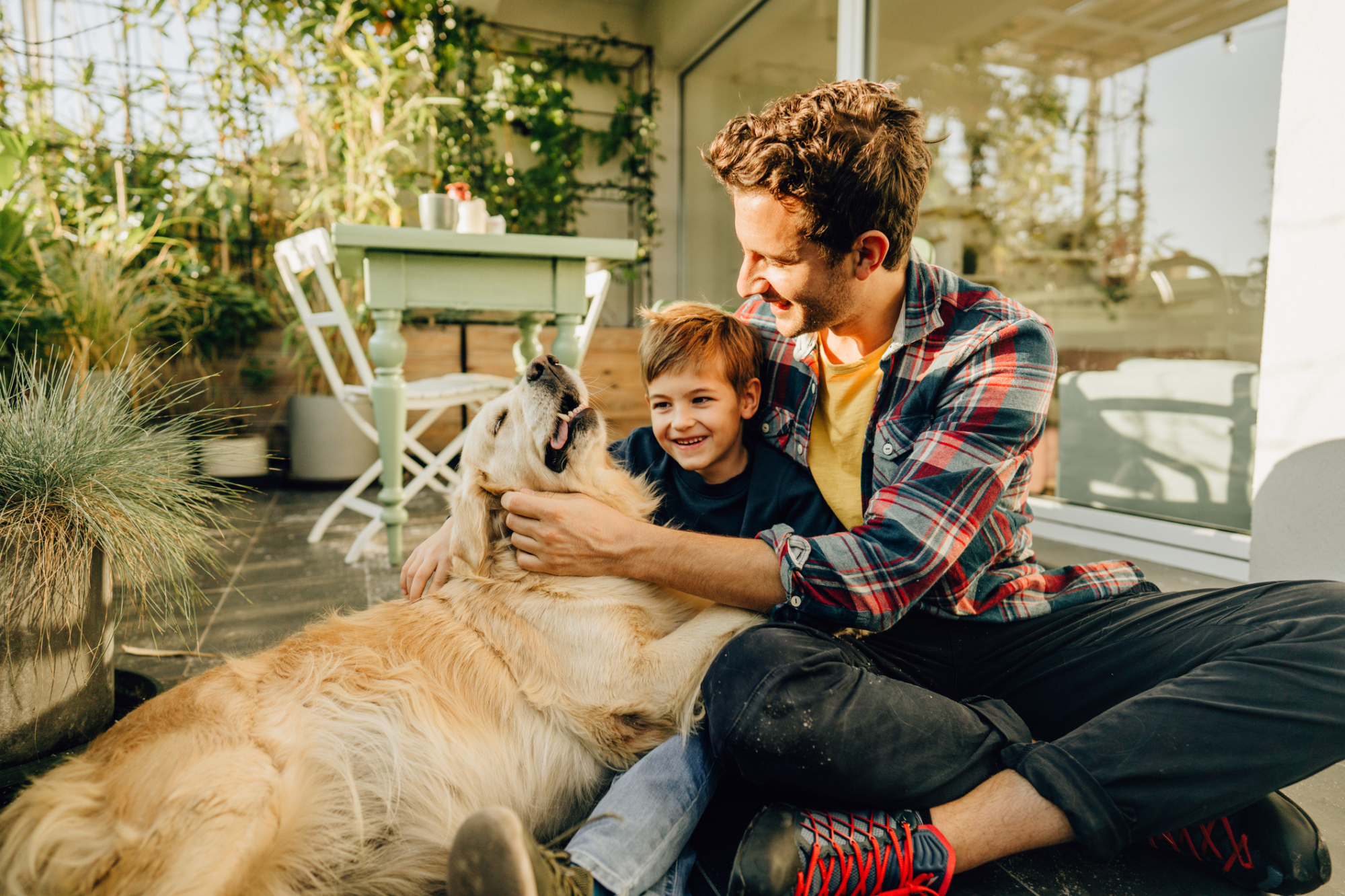 Image d'un père et d'un jeune garçon assis par terre en train de caresser un golden retriever heureux et détendu