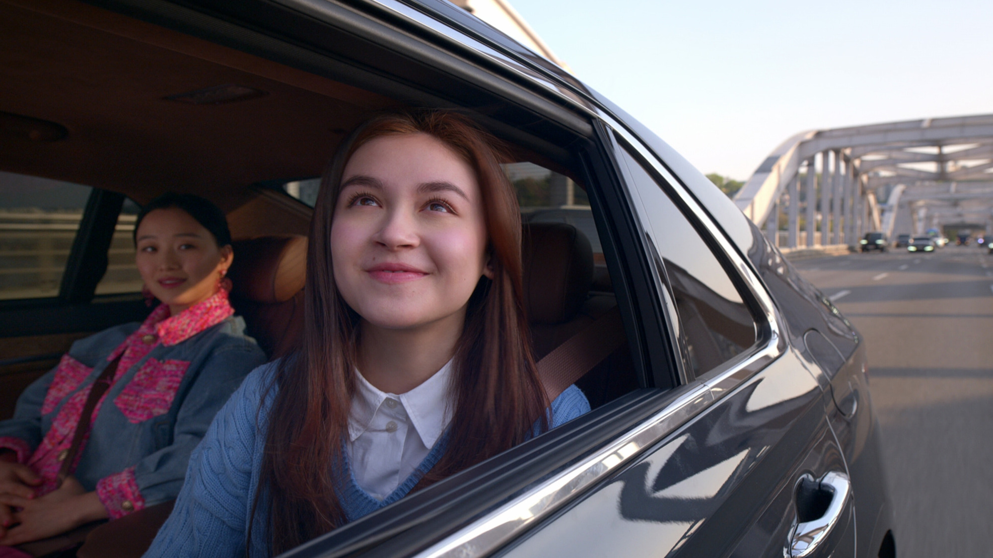 Deux filles sont assises dans une voiture, l'une regarde joyeusement par la fenêtre. 