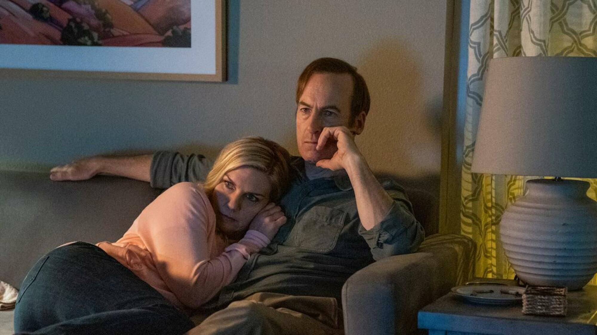 Un couple se blottit sur le canapé, l'air inquiet : Bob Odenkirk dans le rôle de Saul Goodman, Rhea Seehorn dans le rôle de Kim Wexler,