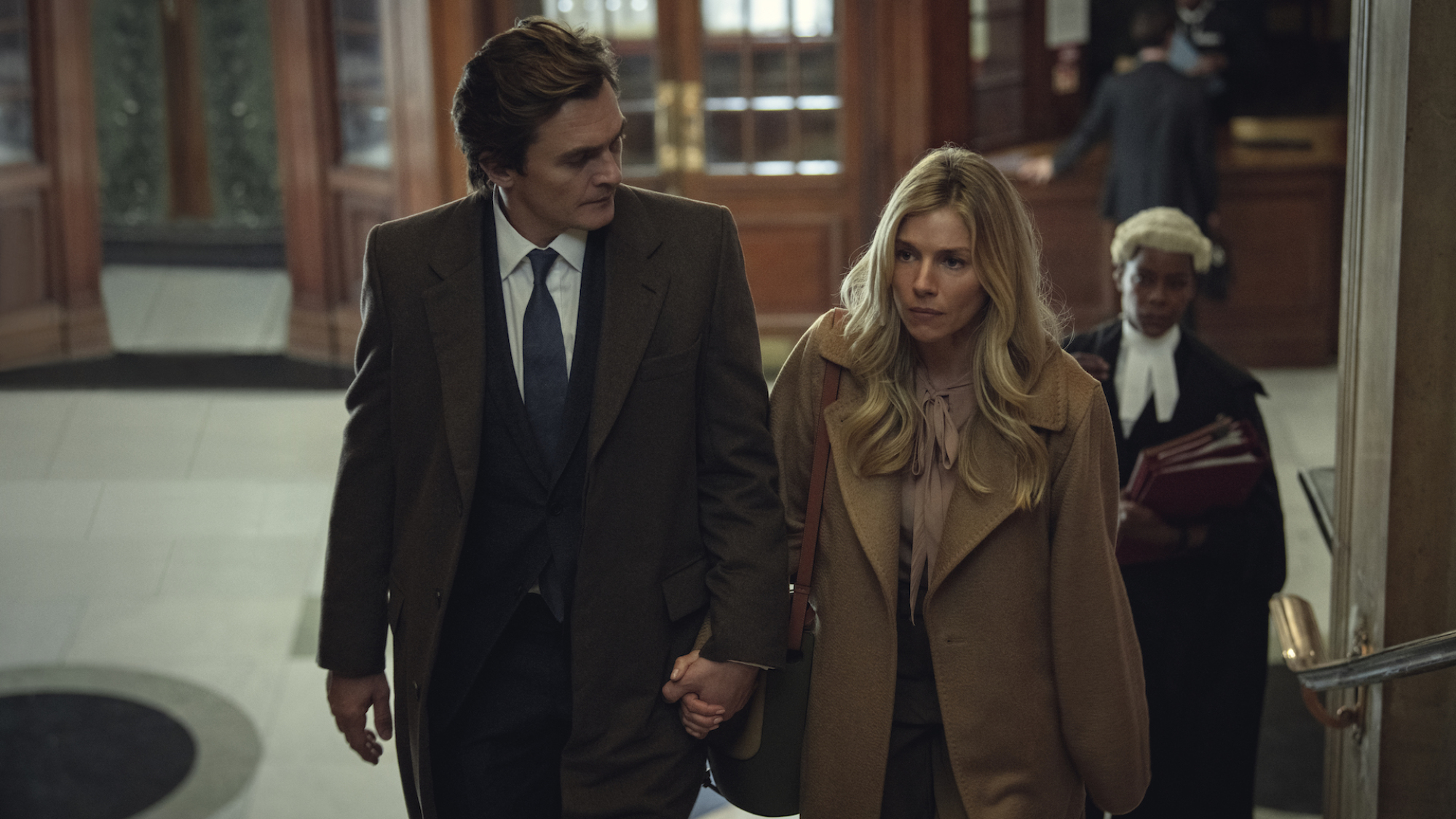 Rupert Friend et Sienna Miller se tiennent la main dans un palais de justice. 