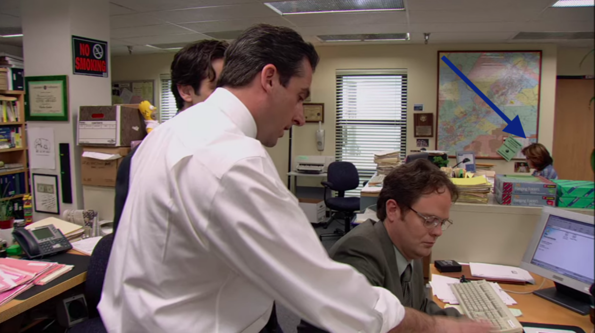 Trois acteurs masculins de The Office se sont blottis autour d'un ordinateur et une flèche pointant vers une femme en arrière-plan.