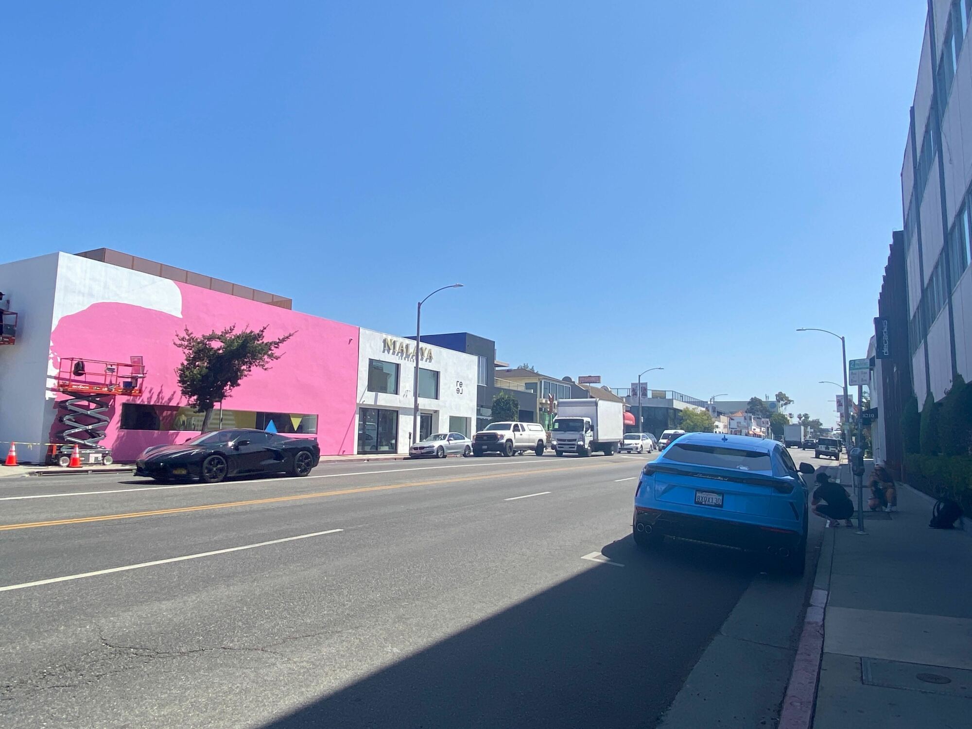 Un bâtiment rose à gauche et une Lamborghini bleue à droite, avec des gens posant devant la voiture.