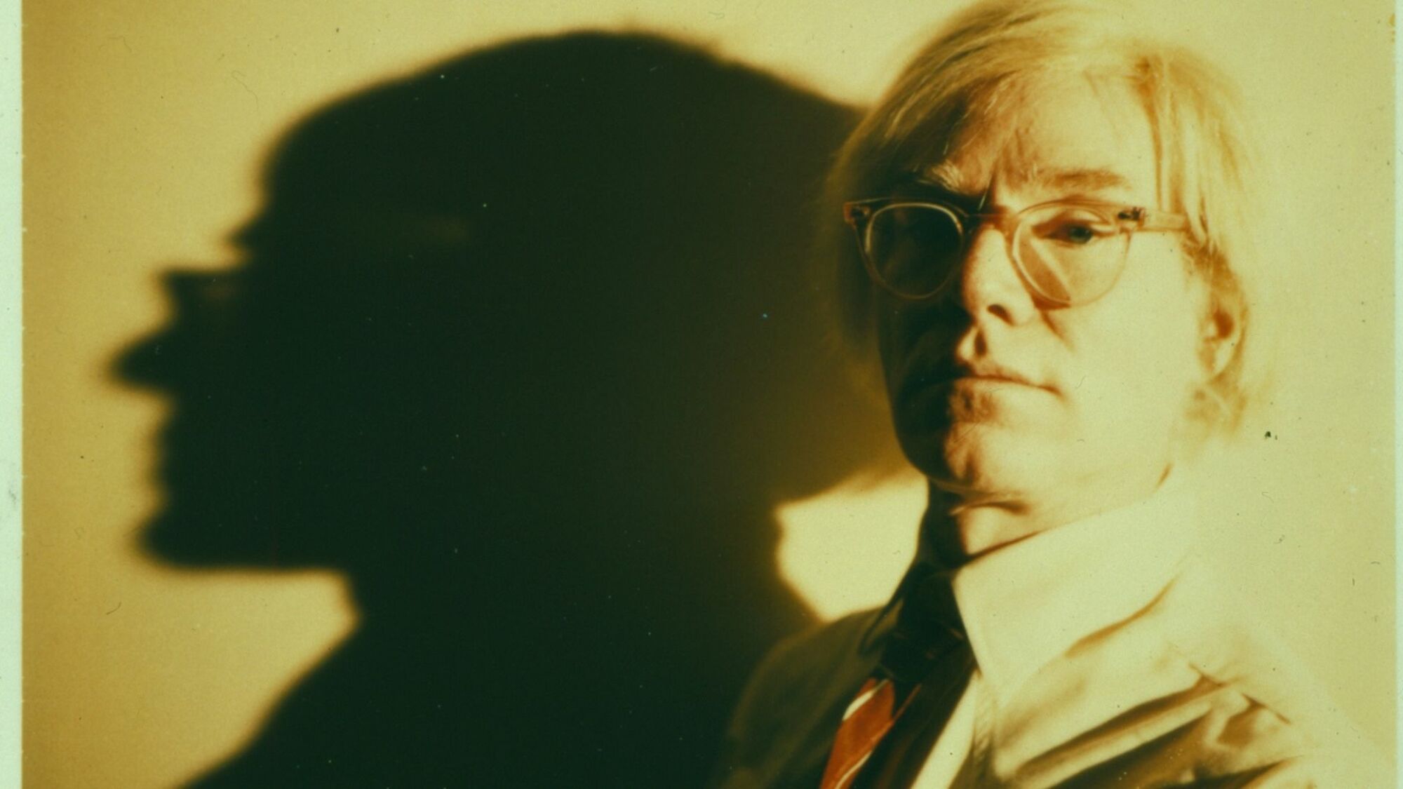 Portrait d'Andy Warhol, avec une grande ombre projetée sur le mur derrière lui.