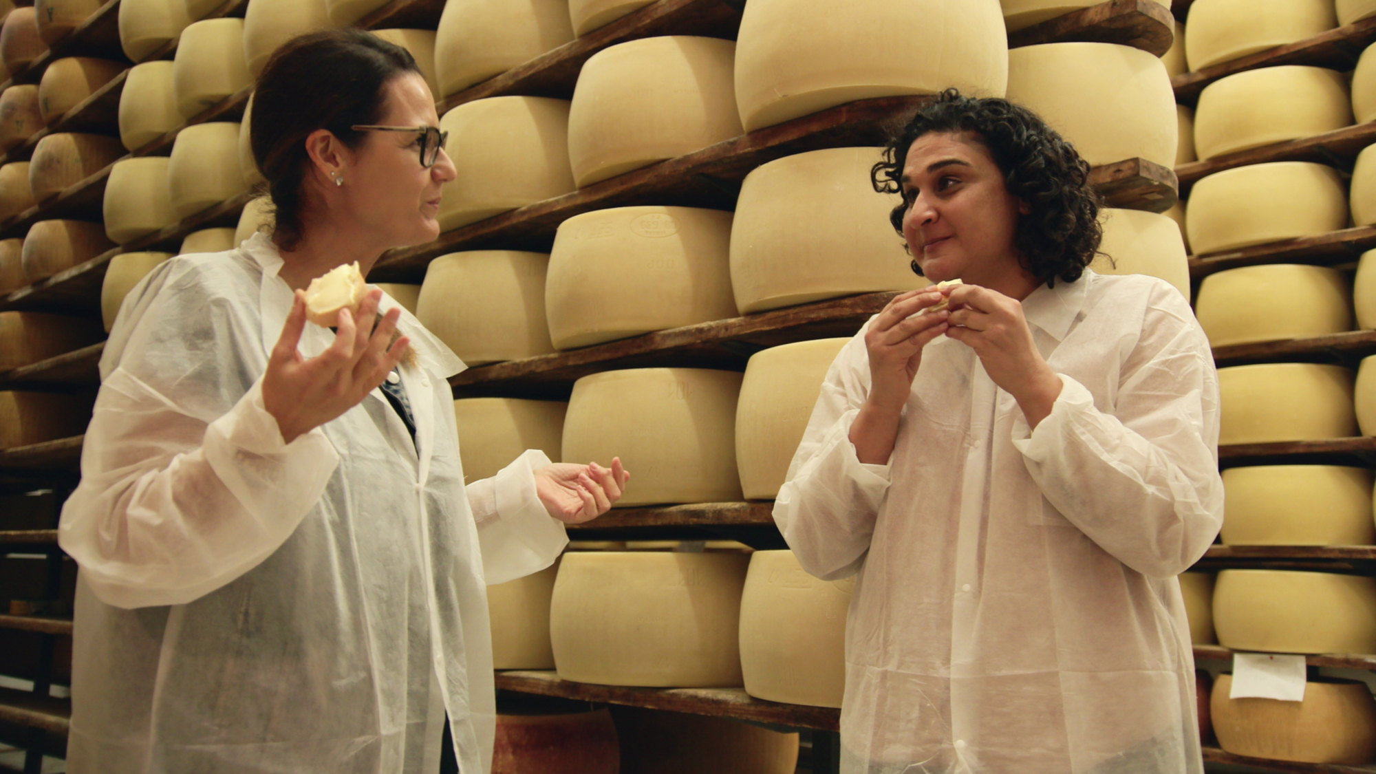 Deux femmes, dont l'animatrice Samin Nosrat, mangent du fromage devant un mur de meules de fromage