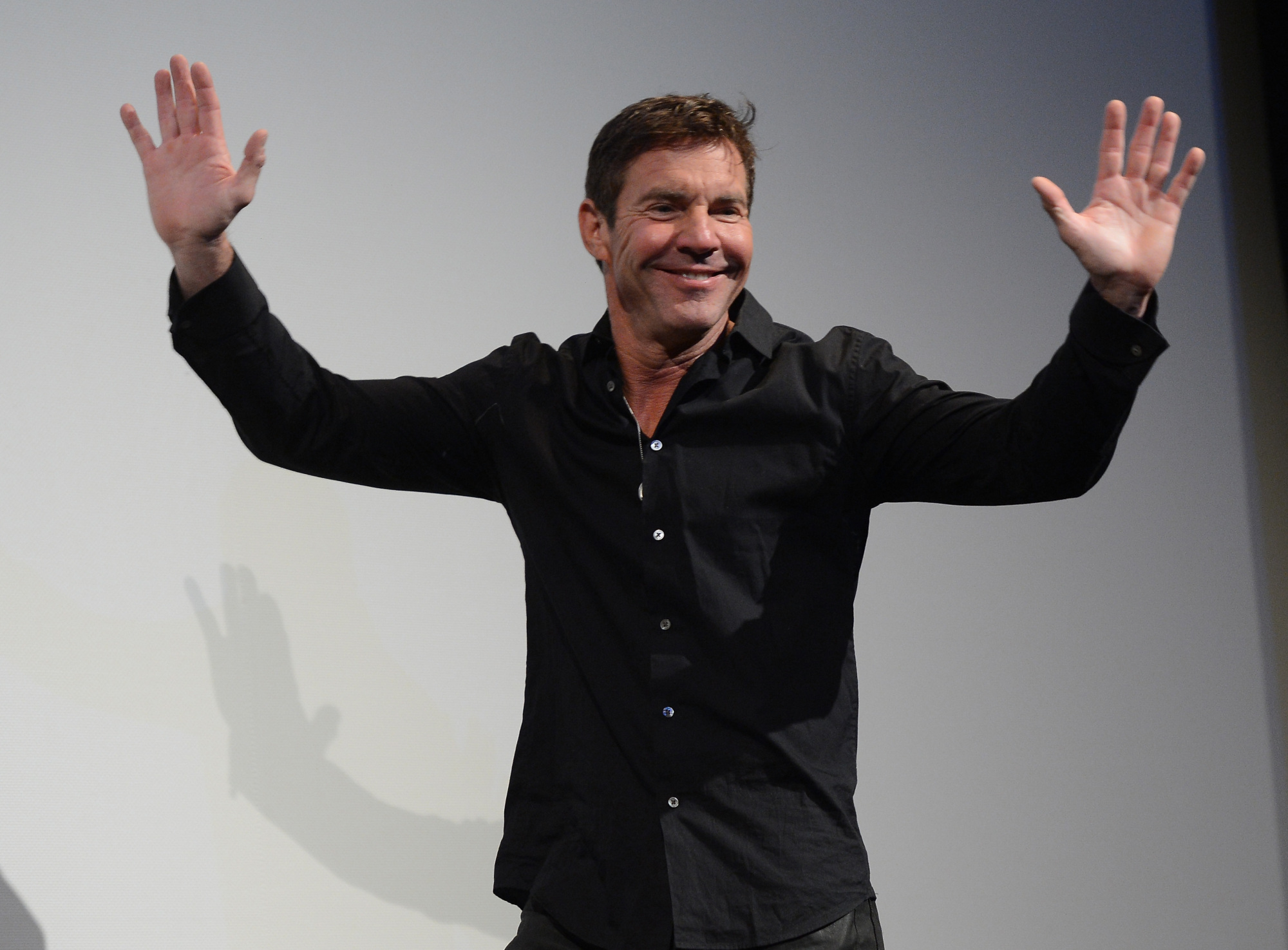 Dennis Quaid avec ses mains levées au-dessus de sa tête. 