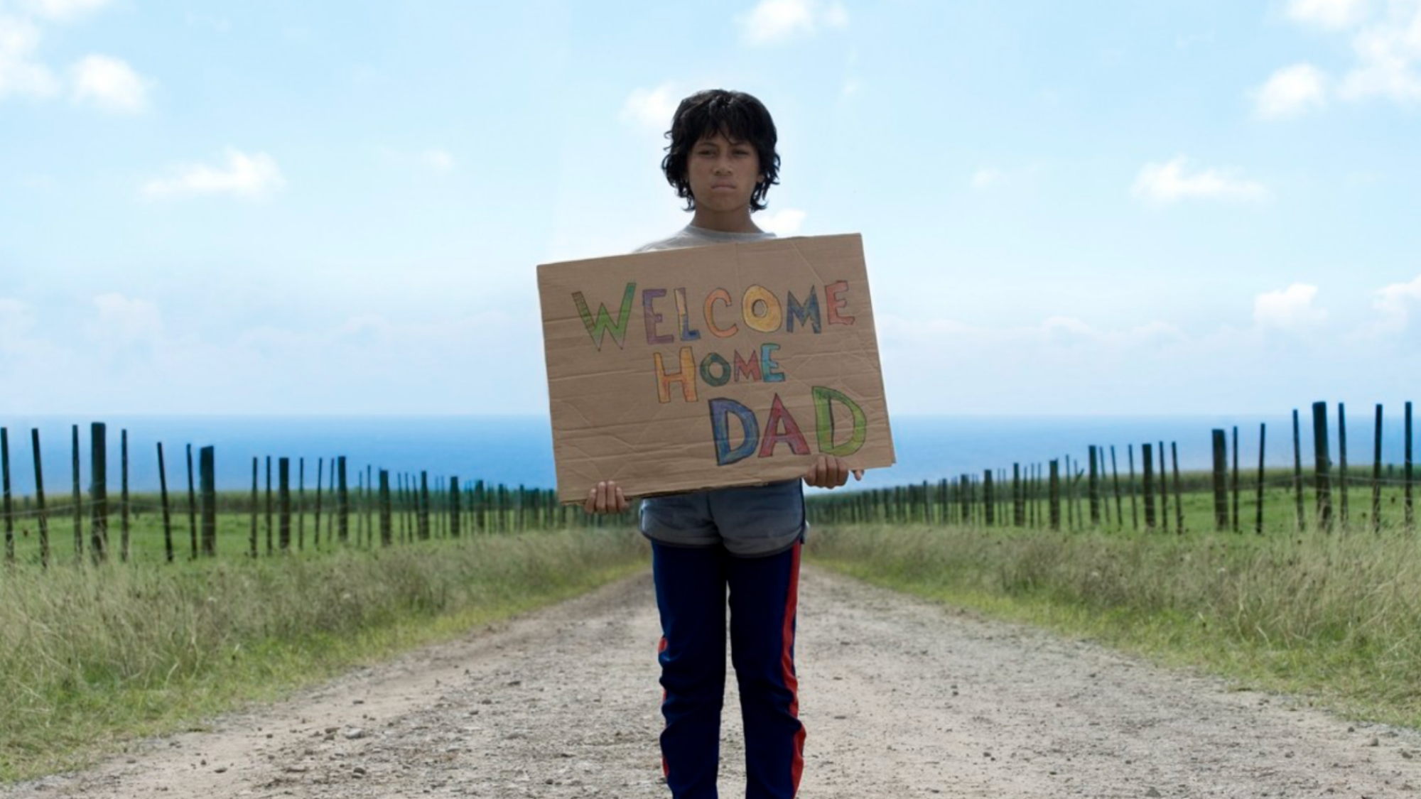 James Rolleston tenant une pancarte indiquant «Bienvenue à la maison papa» pour «Boy»