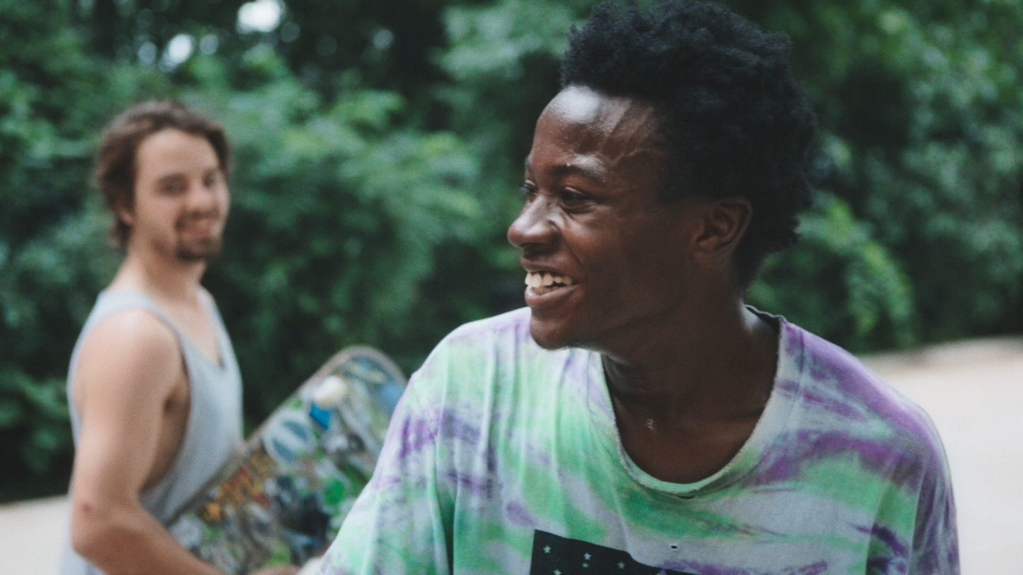 Deux jeunes hommes sourient, leur skateboard à la main. 