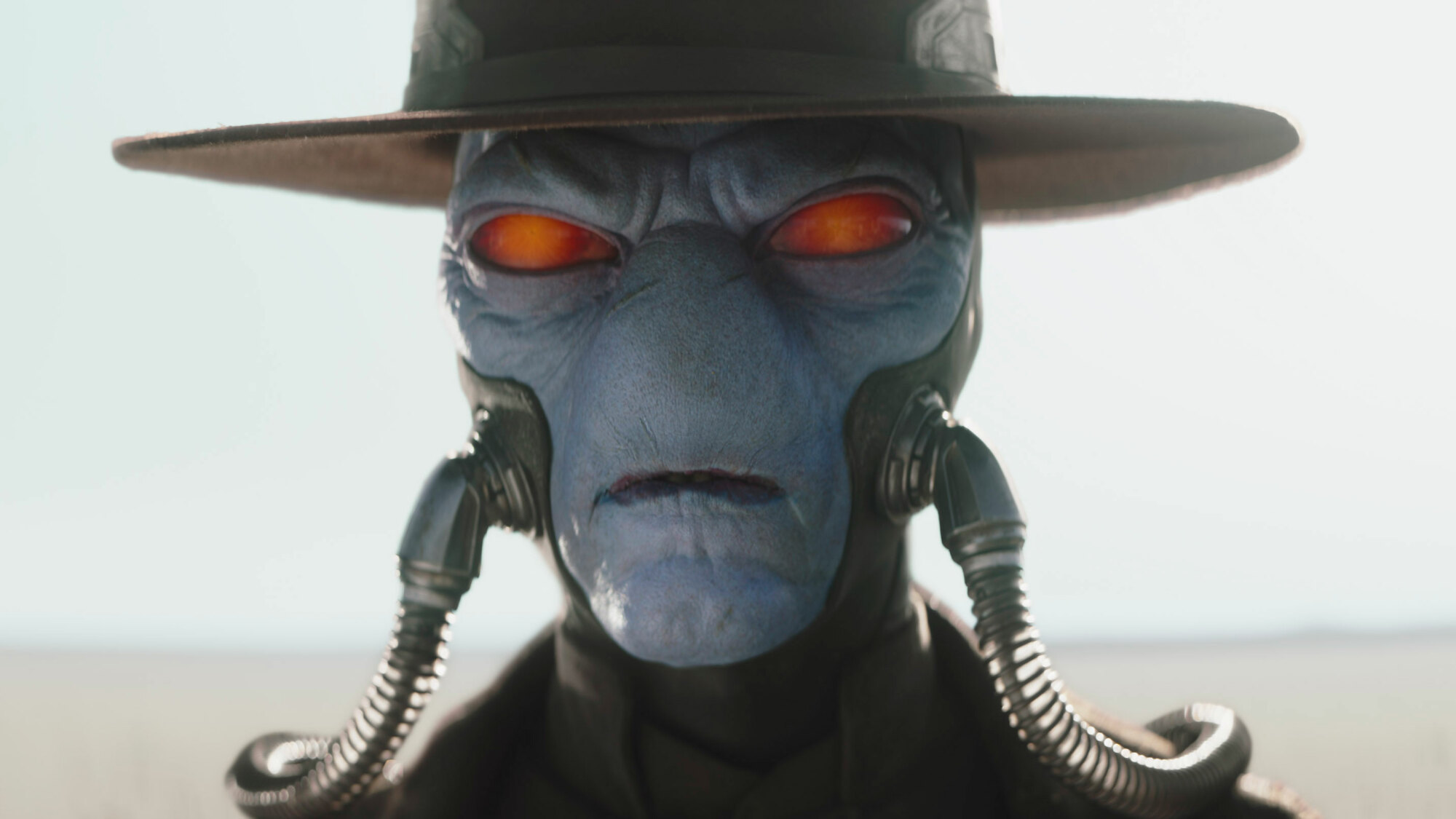Un gros plan du visage d'un extraterrestre à la peau bleue.  Il a les yeux rouges, une fente en guise de bouche et deux tuyaux, apparemment des tubes respiratoires, sortant de ses joues.  C'est une photo de "Le livre de Boba Fett" et le personnage est Cad Bane.