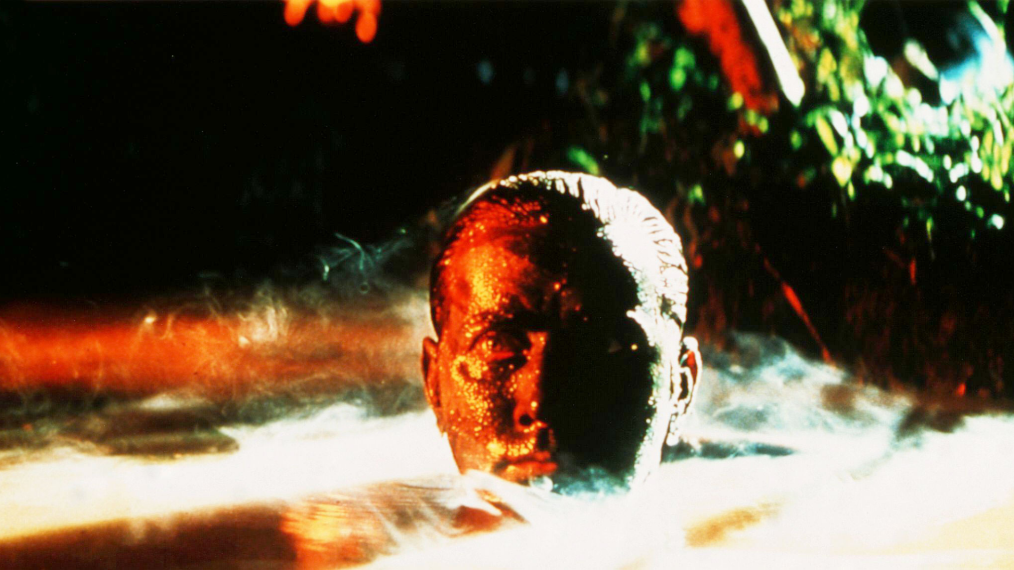 Un homme blanc avec des peintures de guerre sur le visage sort d'un lagon. 