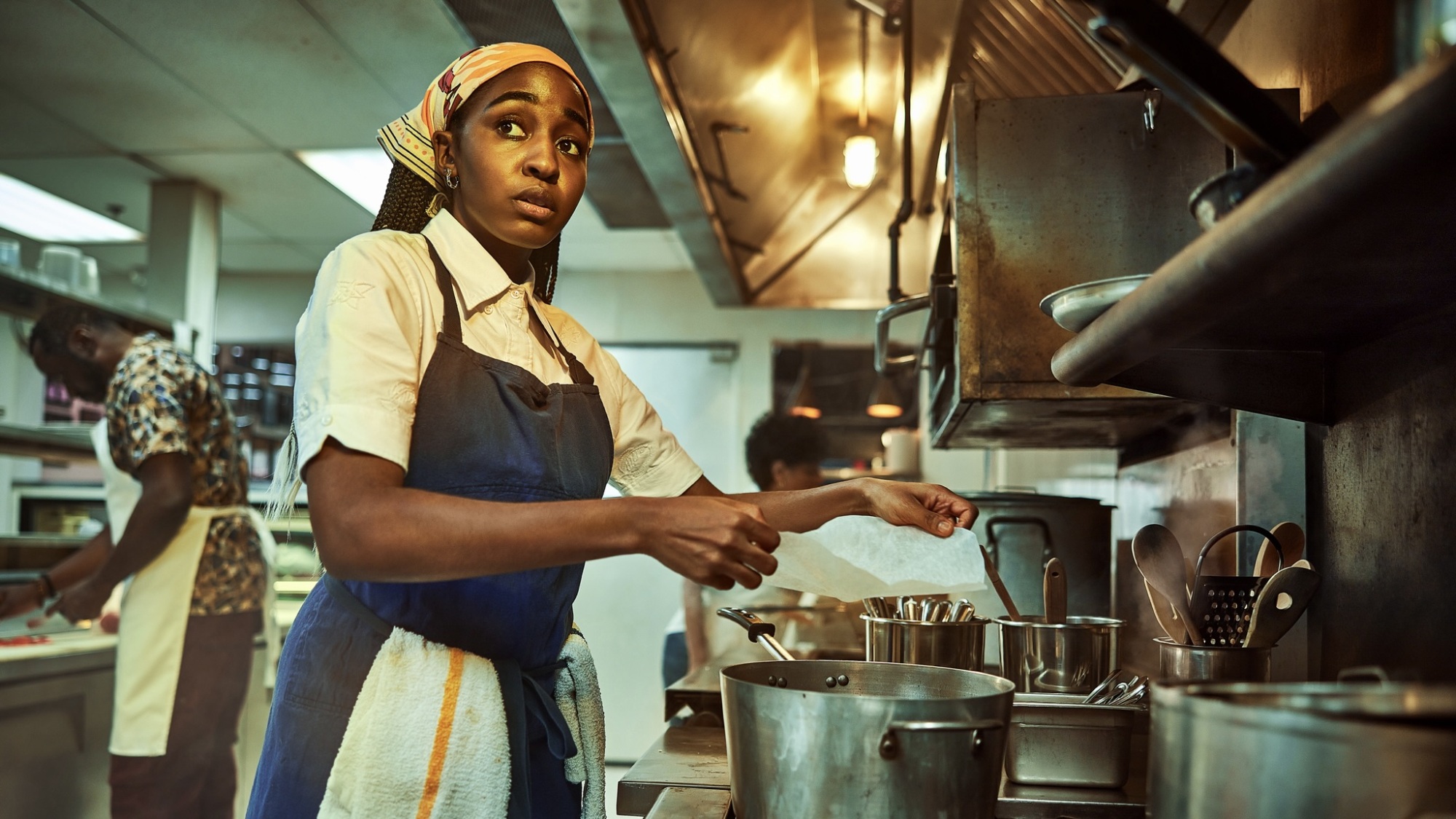 Une femme en tablier bleu tient un filtre en papier au-dessus d'une casserole sur une cuisinière dans un restaurant de cuisine.