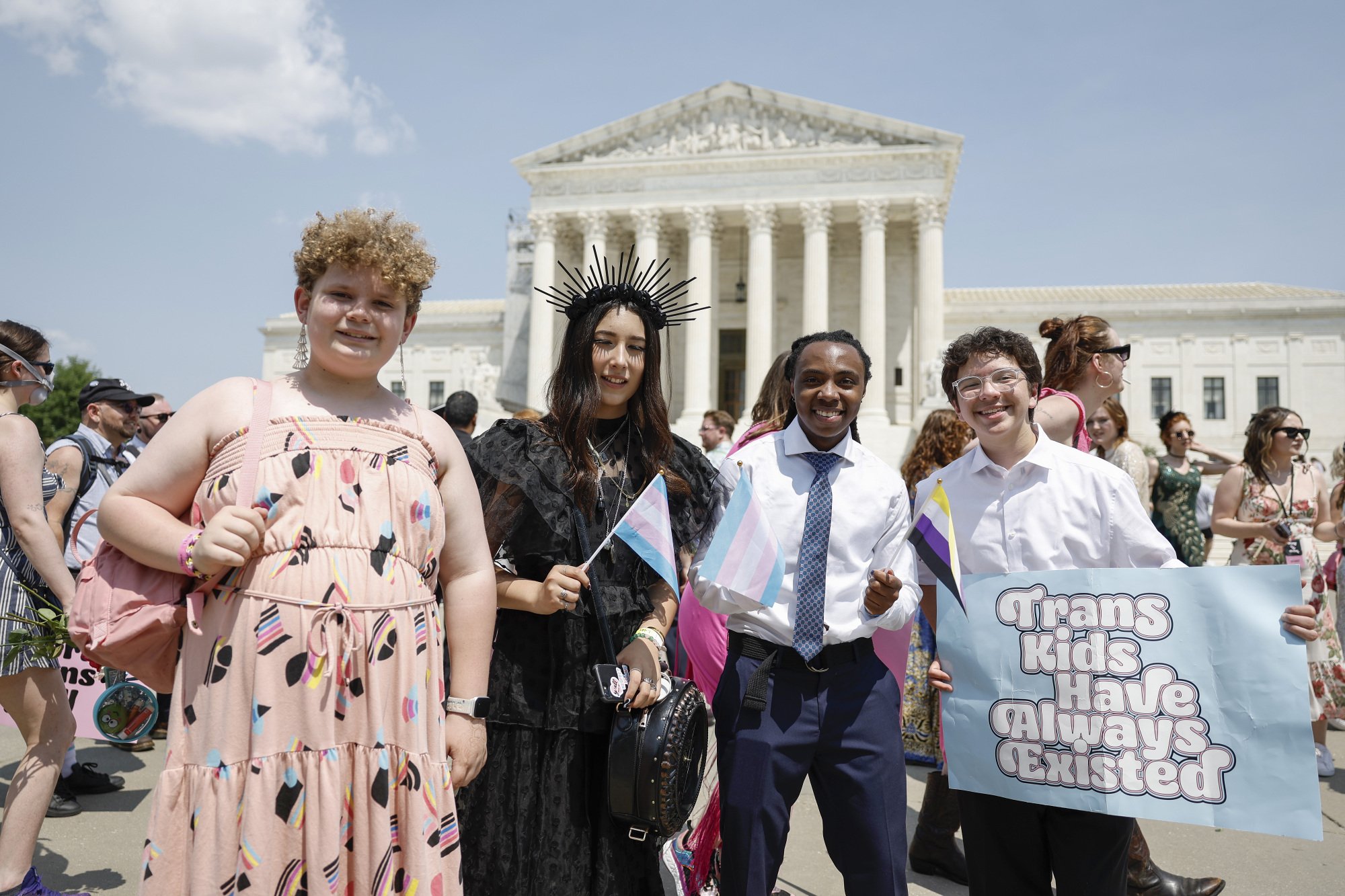 Un groupe de quatre jeunes en tenue de soirée se tient devant le bâtiment de la Cour suprême des États-Unis.  L'un d'eux tient une pancarte qui dit, 