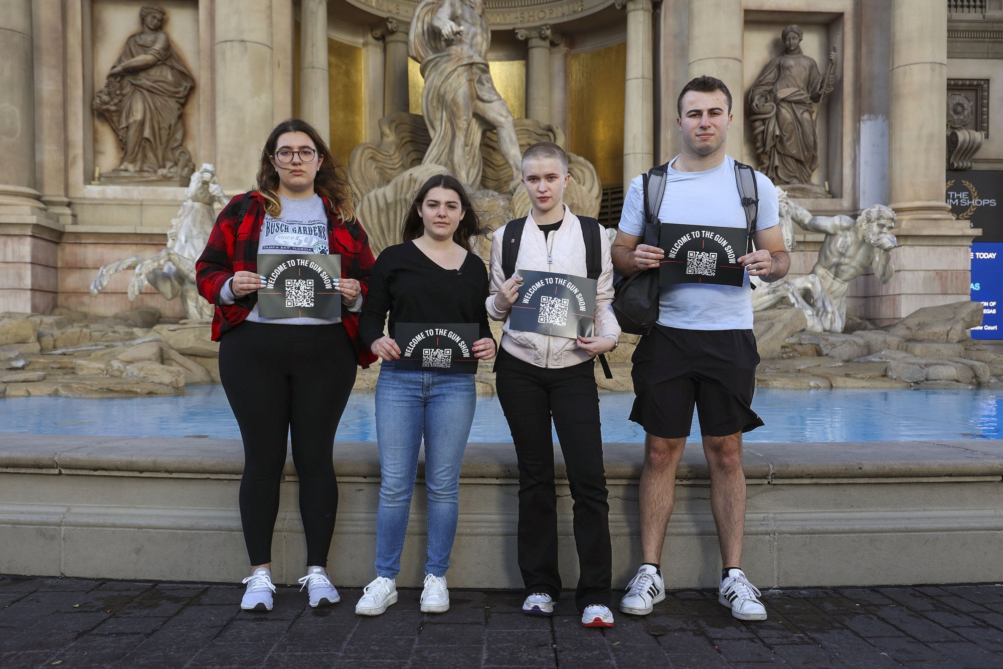 Un groupe de quatre adolescents se tient devant une fontaine à Las Vegas.  Ils brandissent des pancartes noires qui disent 