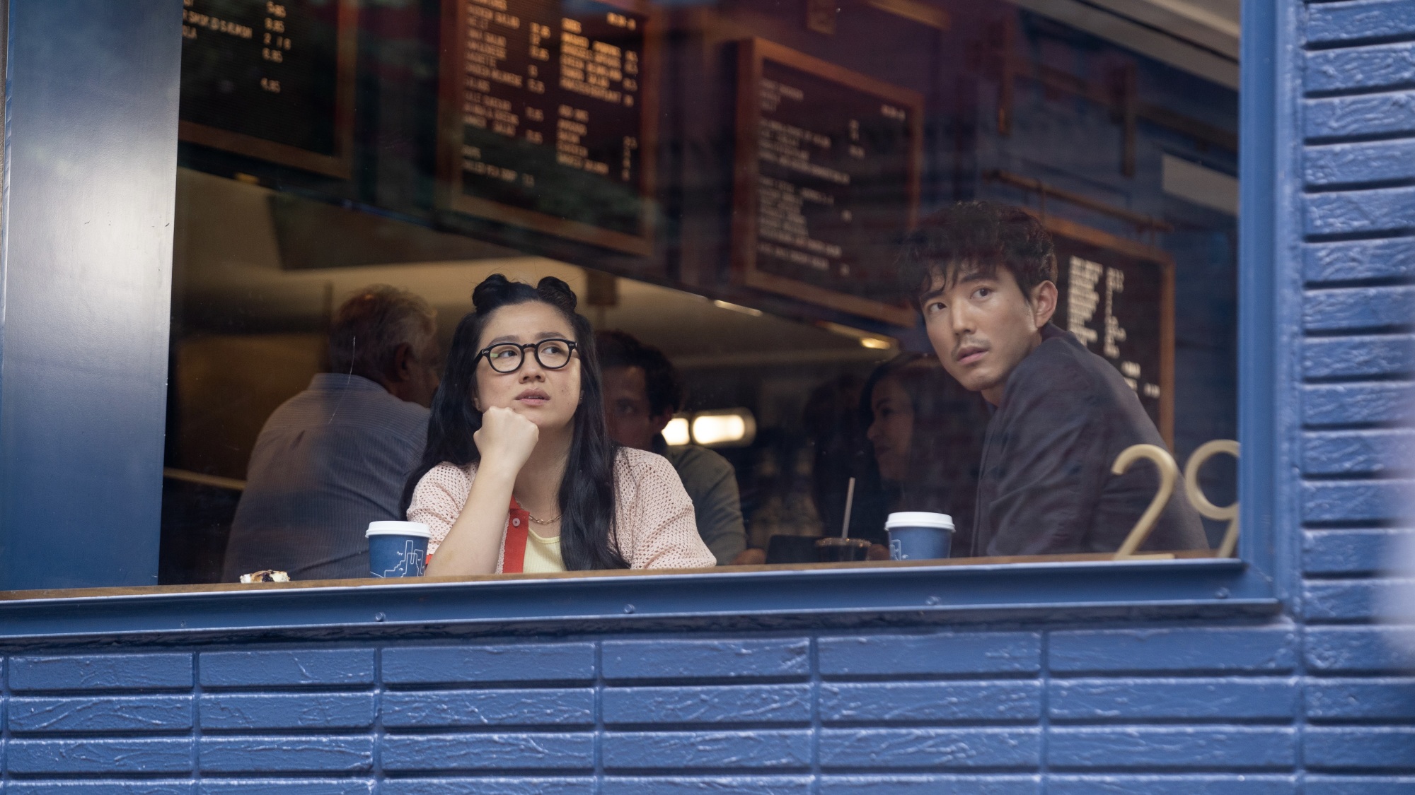 Un homme et une femme regardent par la fenêtre d'un café à l'extérieur en briques bleues.