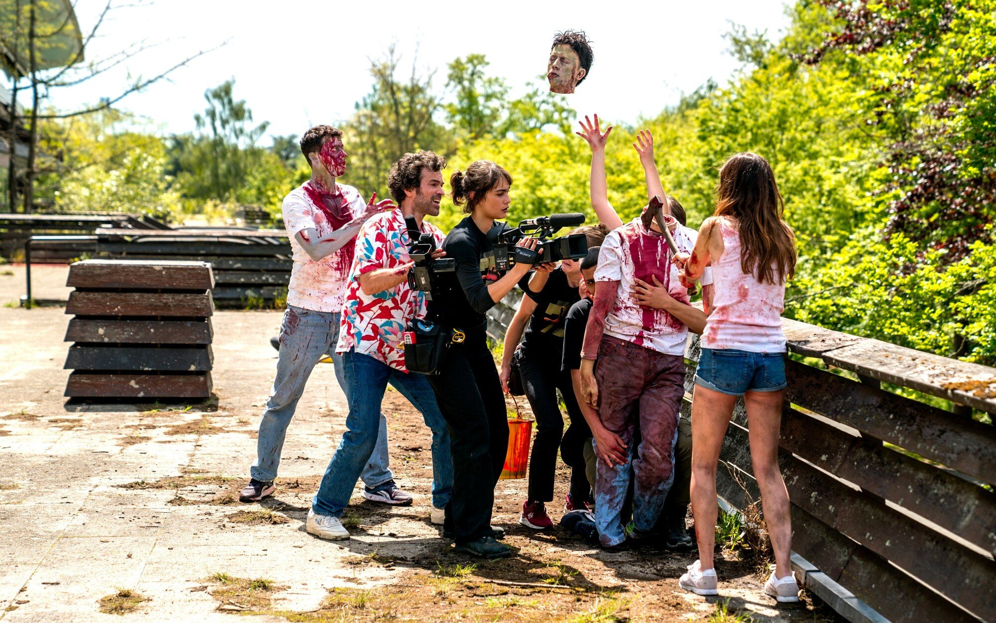 Un groupe d'acteurs et de membres de l'équipe d'un film de zombies lancent une fausse tête en l'air pendant le tournage d'une scène.