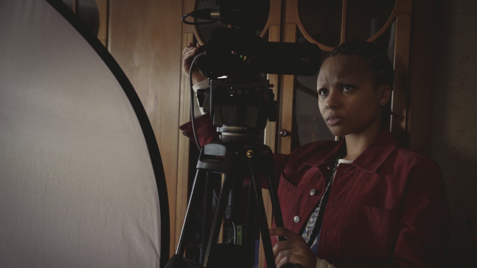 Une jeune femme en chemise rouge se tient derrière une caméra.