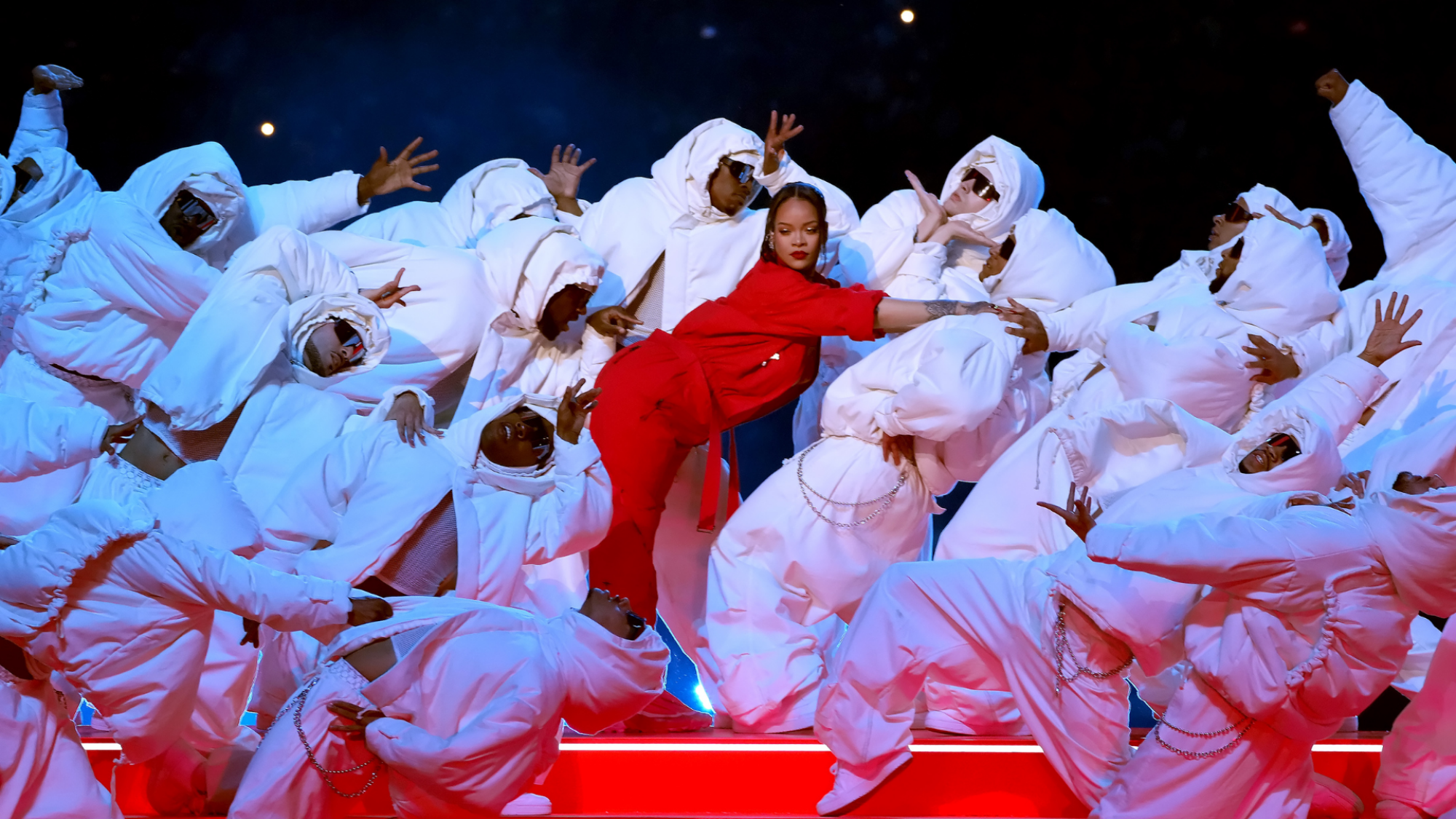 Rihanna, en rouge, au centre d'un tableau de danseuses de réserve, vêtues de blanc.