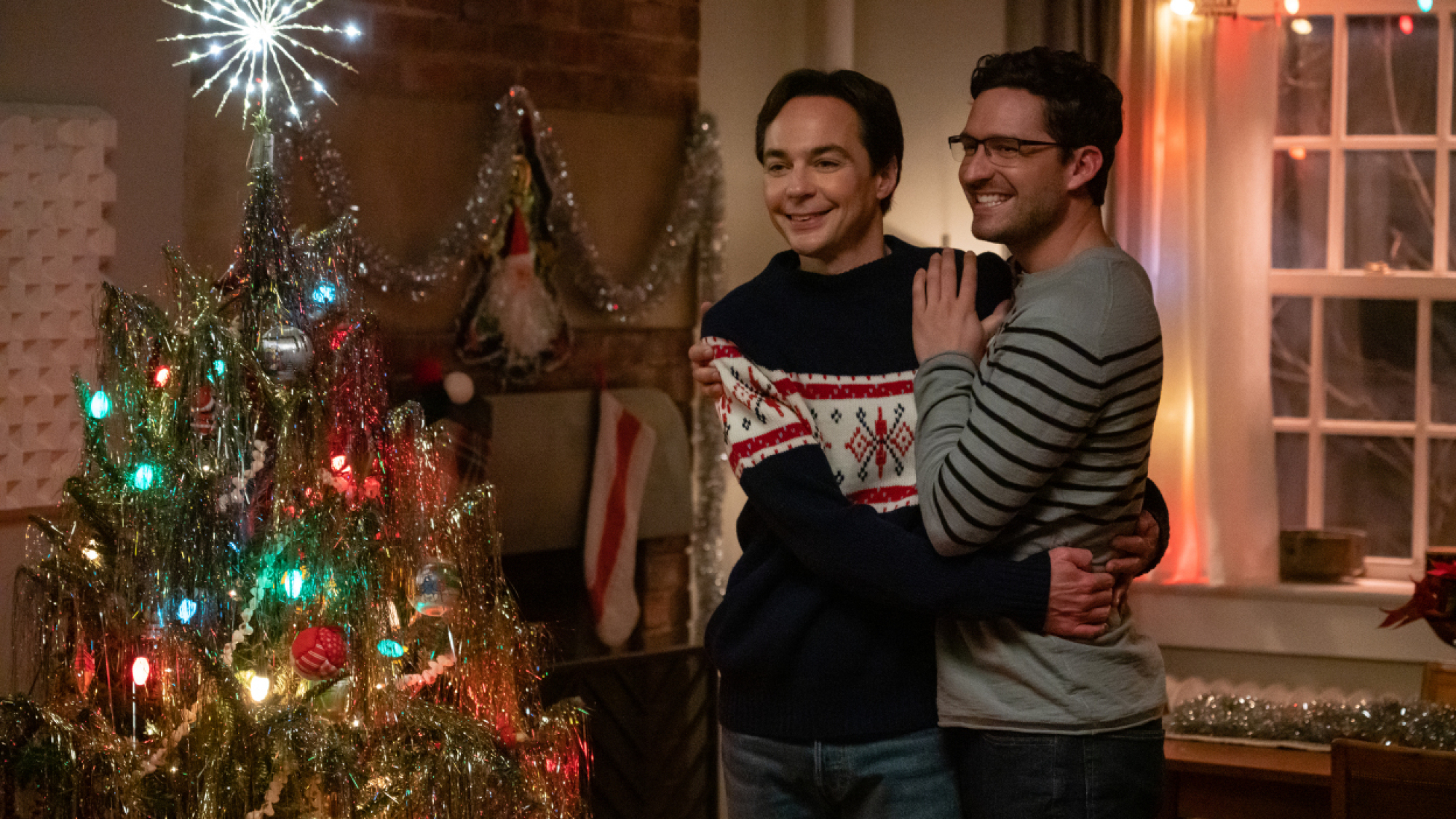 Deux hommes s'embrassent devant un sapin de Noël. 