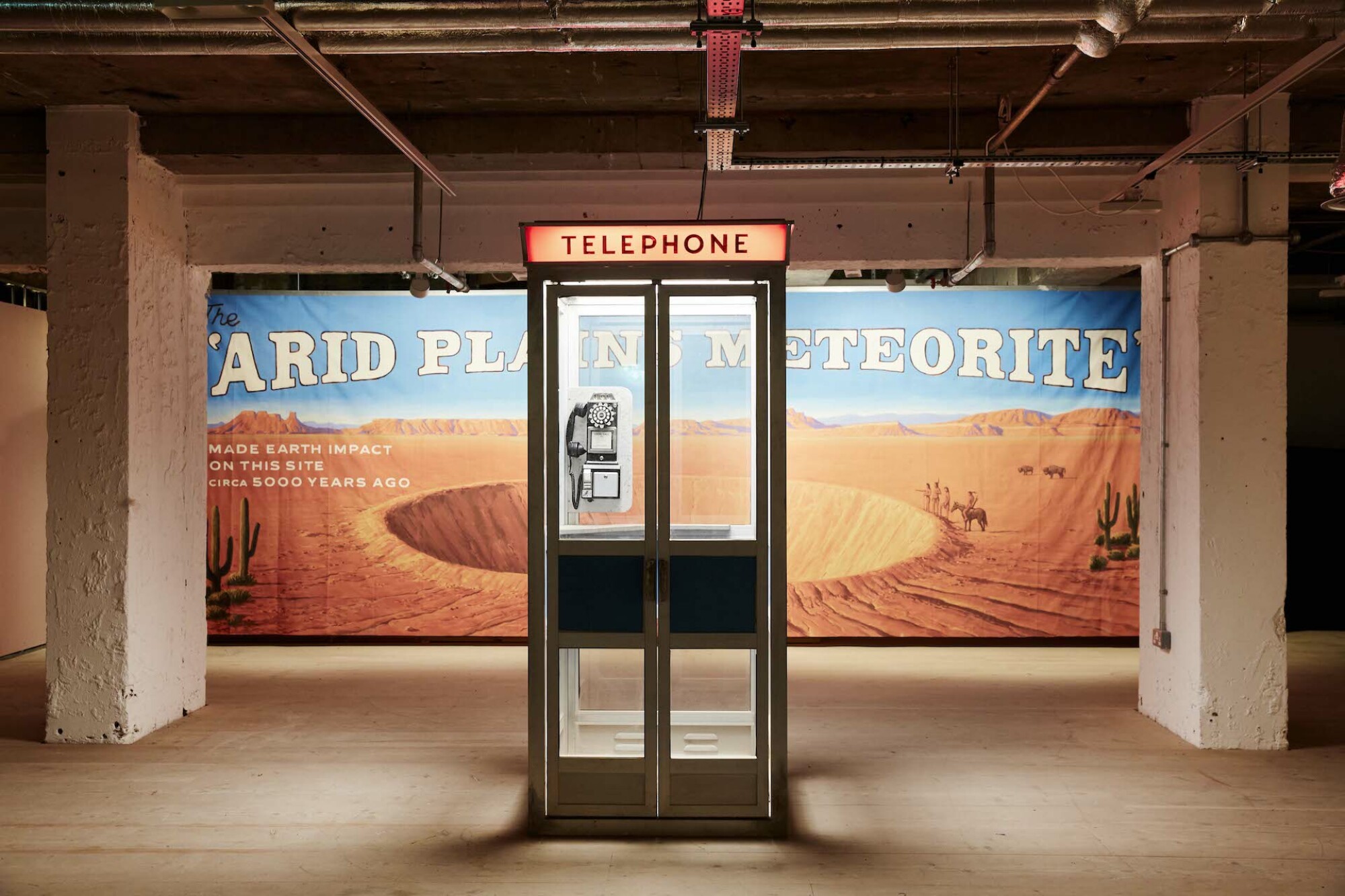 Dans l'exposition 'Asteroid City' à Londres, une cabine téléphonique devant une publicité pour un cratère.