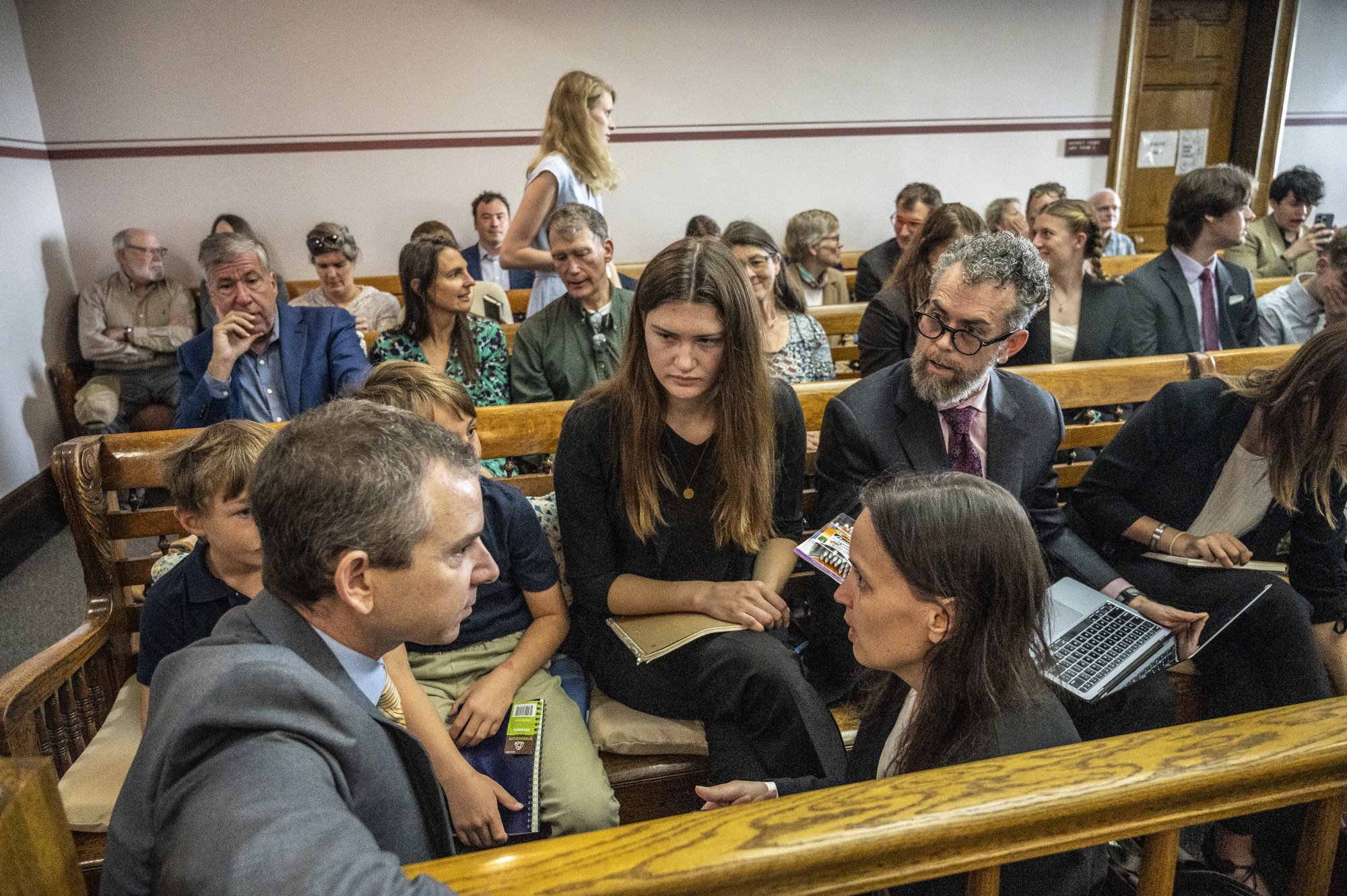 Un groupe de plaignants et d'avocats s'assoient et conversent dans une salle d'audience.