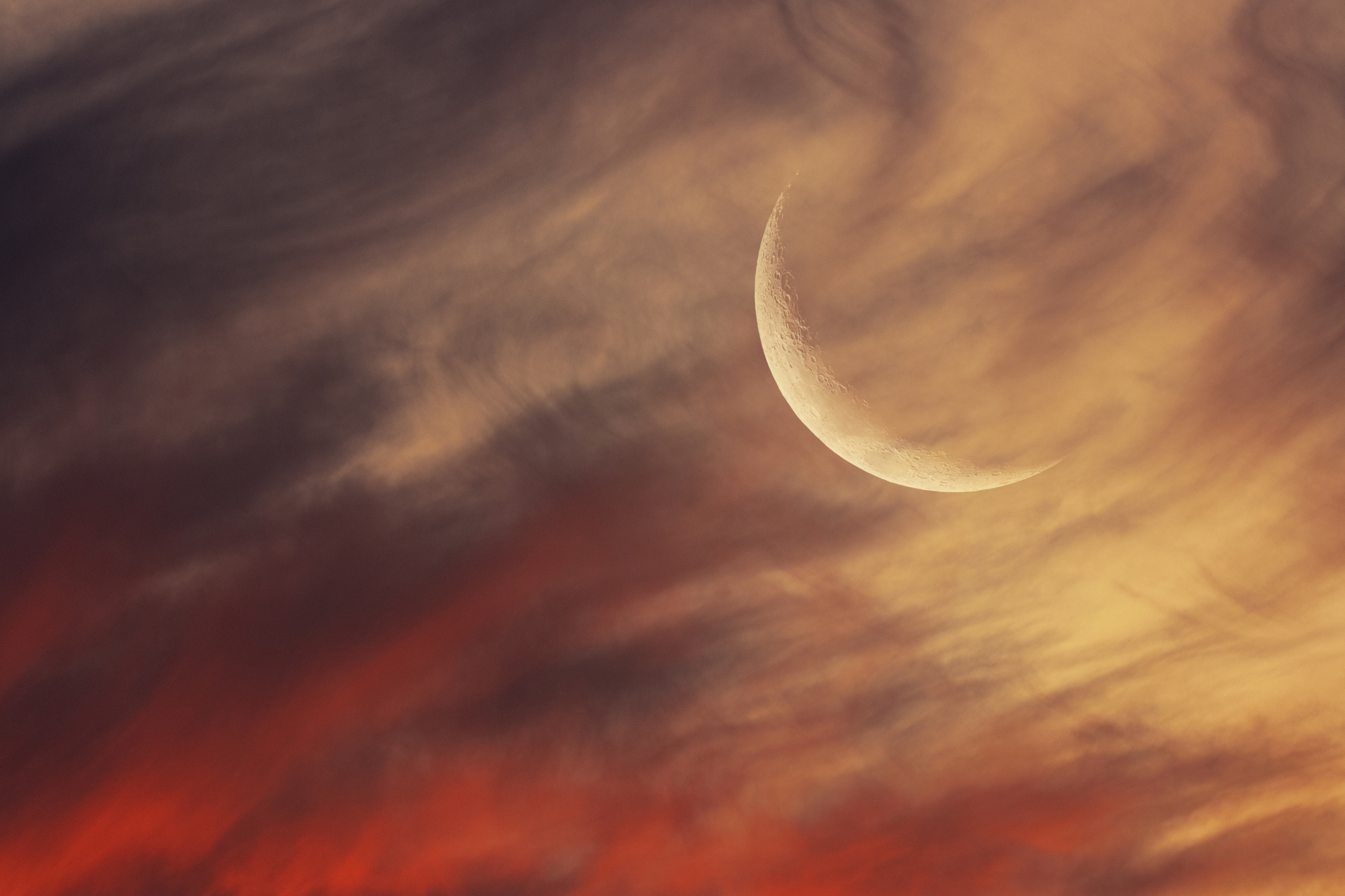 Un croissant de lune visible dans un ciel rouge et orange.