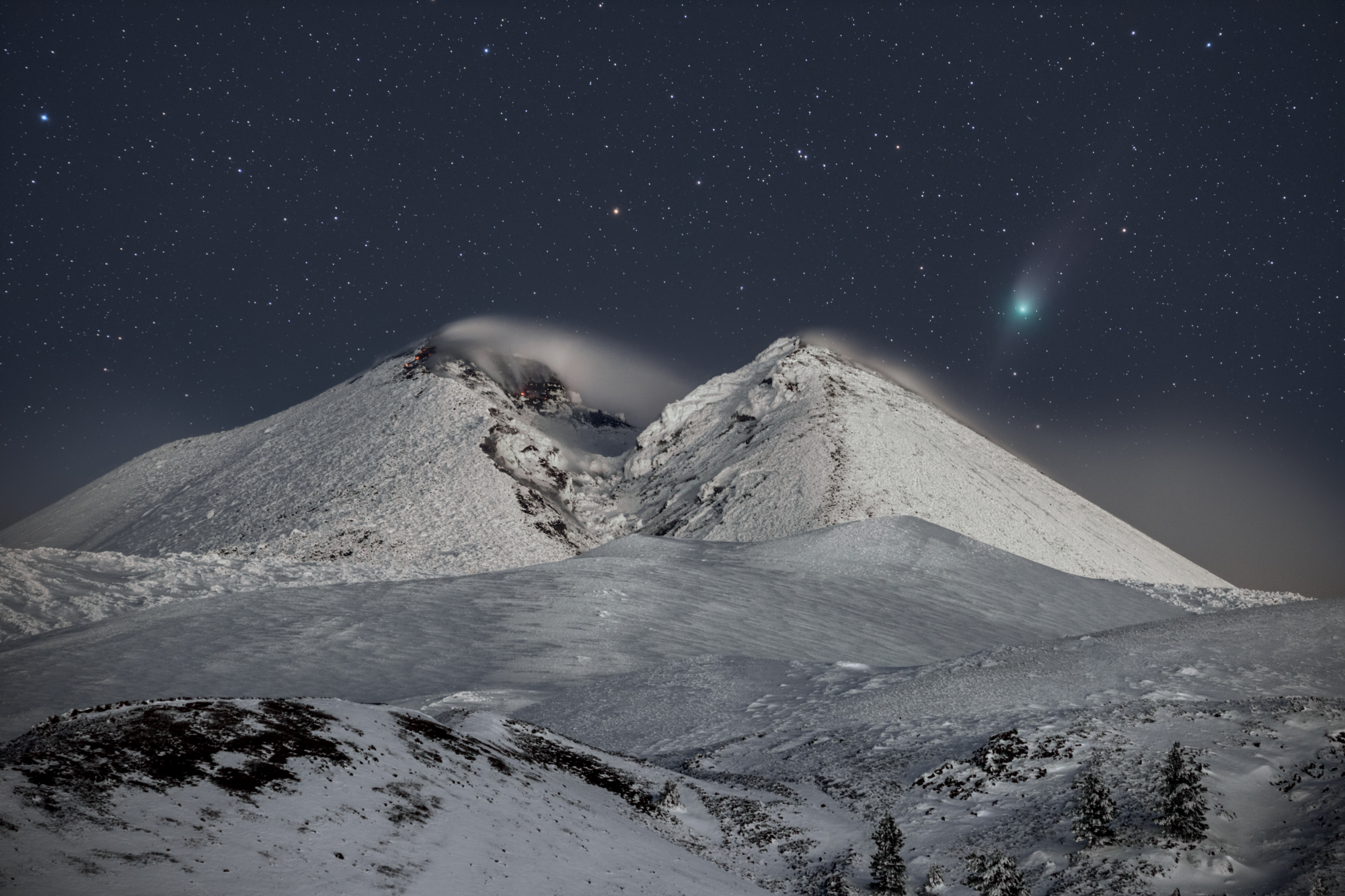 Une comète visible au-dessus d'une montagne enneigée.