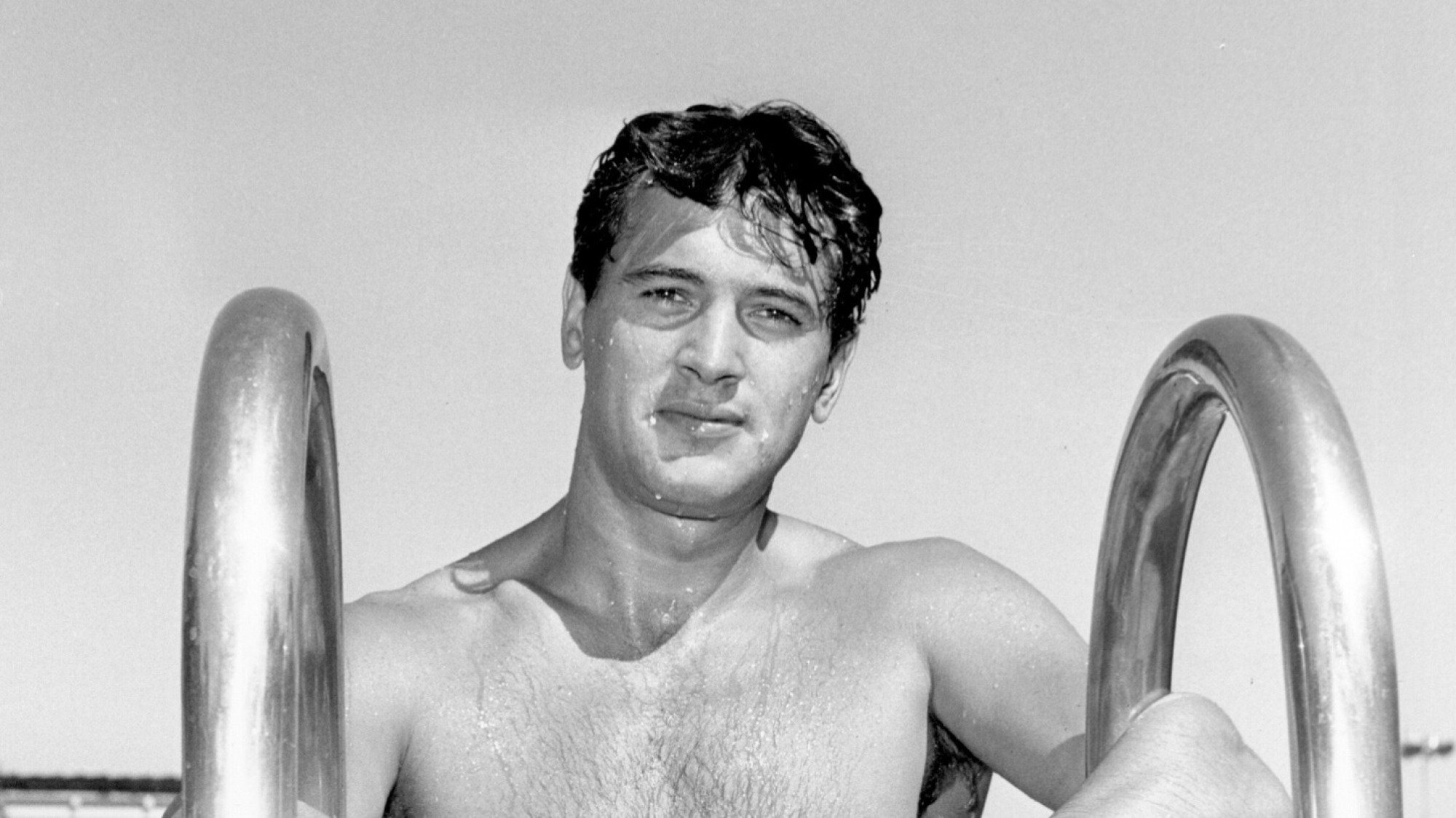 Une image en noir et blanc d'un homme souriant près d'une piscine. 