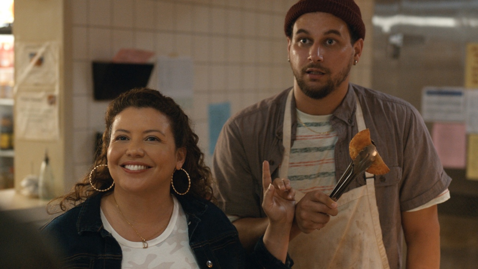 Une femme et un homme sourient en préparant des empanadas et en parlant à un client. 