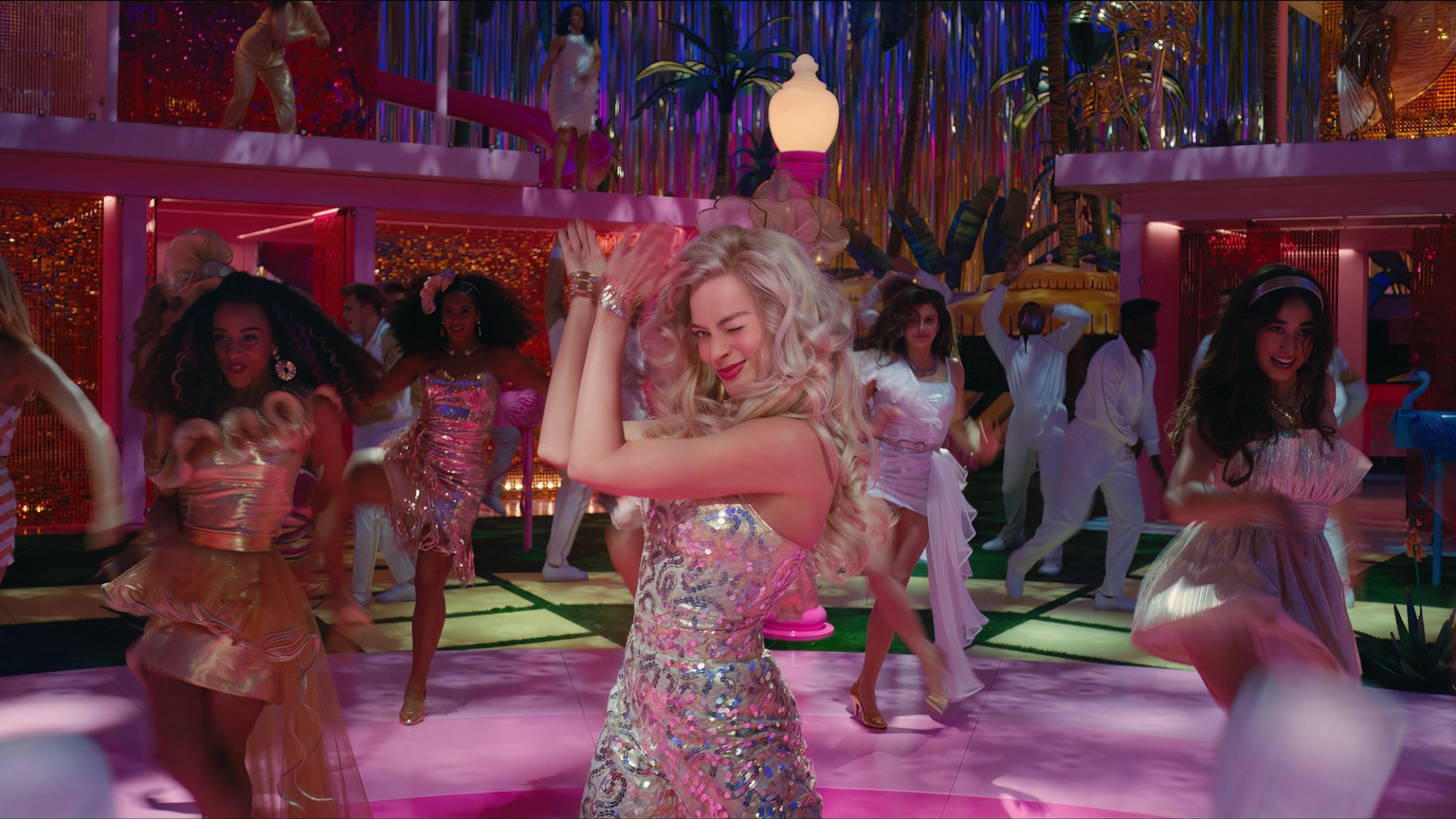 Margot Robbie dans une séquence de danse disco colorée, faisant un clin d'œil à la caméra et applaudissant, dans le film 