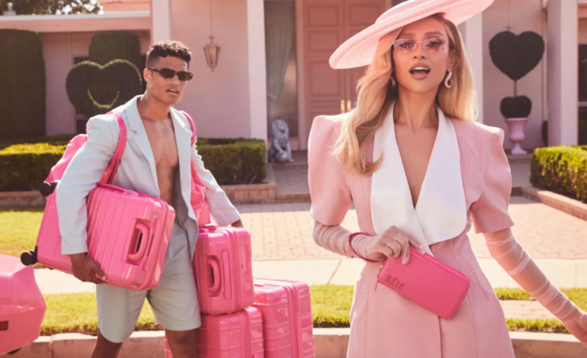 Deux personnes tenant des bagages roses sur le thème de Barbie et un portefeuille avec une maison en arrière-plan