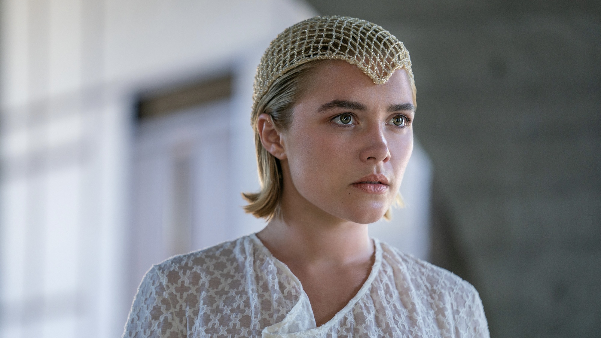 Une femme aux cheveux mi-longs vêtue d'une robe blanche et d'un filet doré couvrant le haut de sa tête.