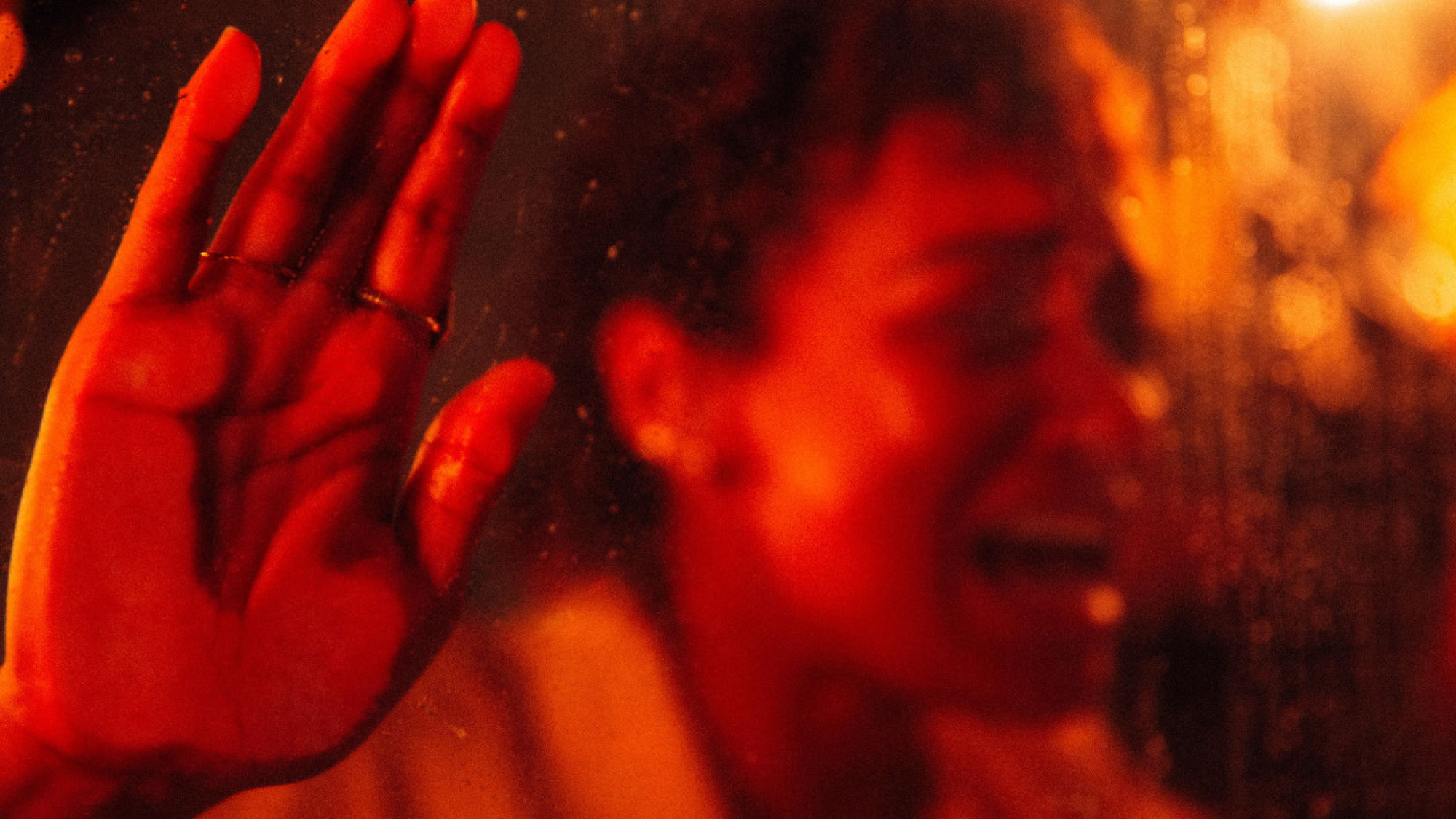 Une femme appuie sa main contre une vitre dans une pièce rouge. 