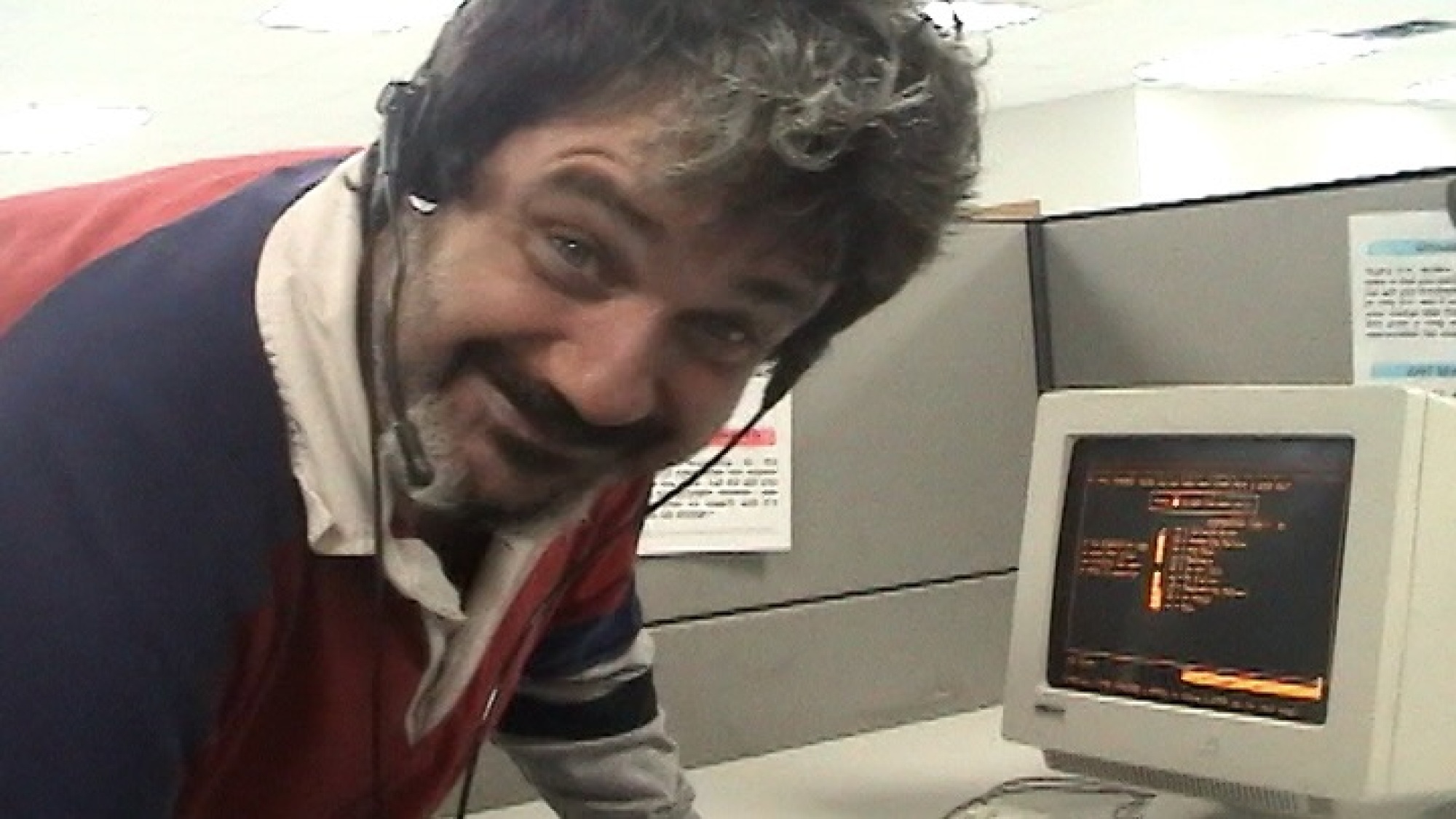 Un homme dans un casque devant un ordinateur avec un écran noir et du texte orange dessus.