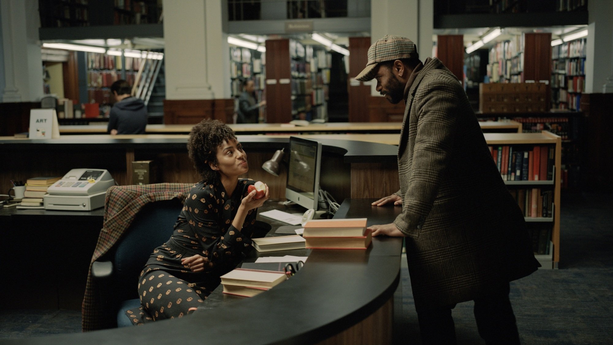 Un homme se penche au-dessus d’un bureau de bibliothèque et parle à la femme assise derrière.