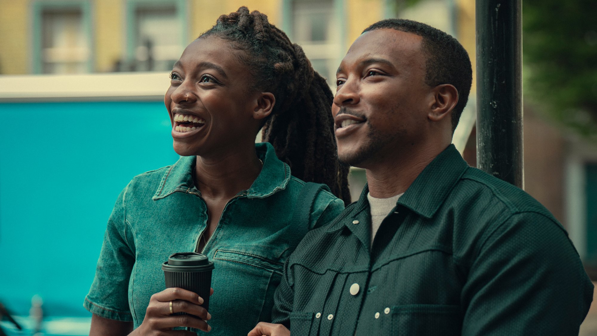 Simbi Ajikawo et Ashley Walters se tiennent bras dessus bras dessous, souriant et tenant un café dans l