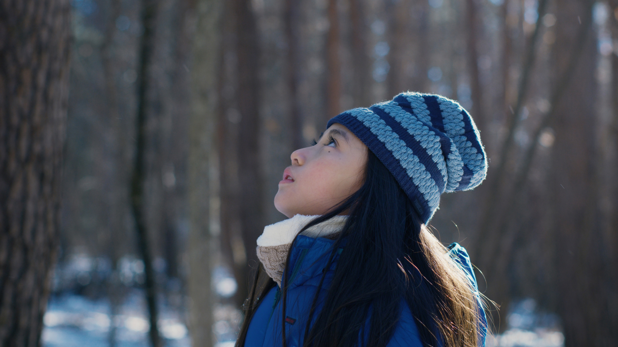 Une jeune fille en vêtements d'hiver se tient dans un bois et regarde le ciel.