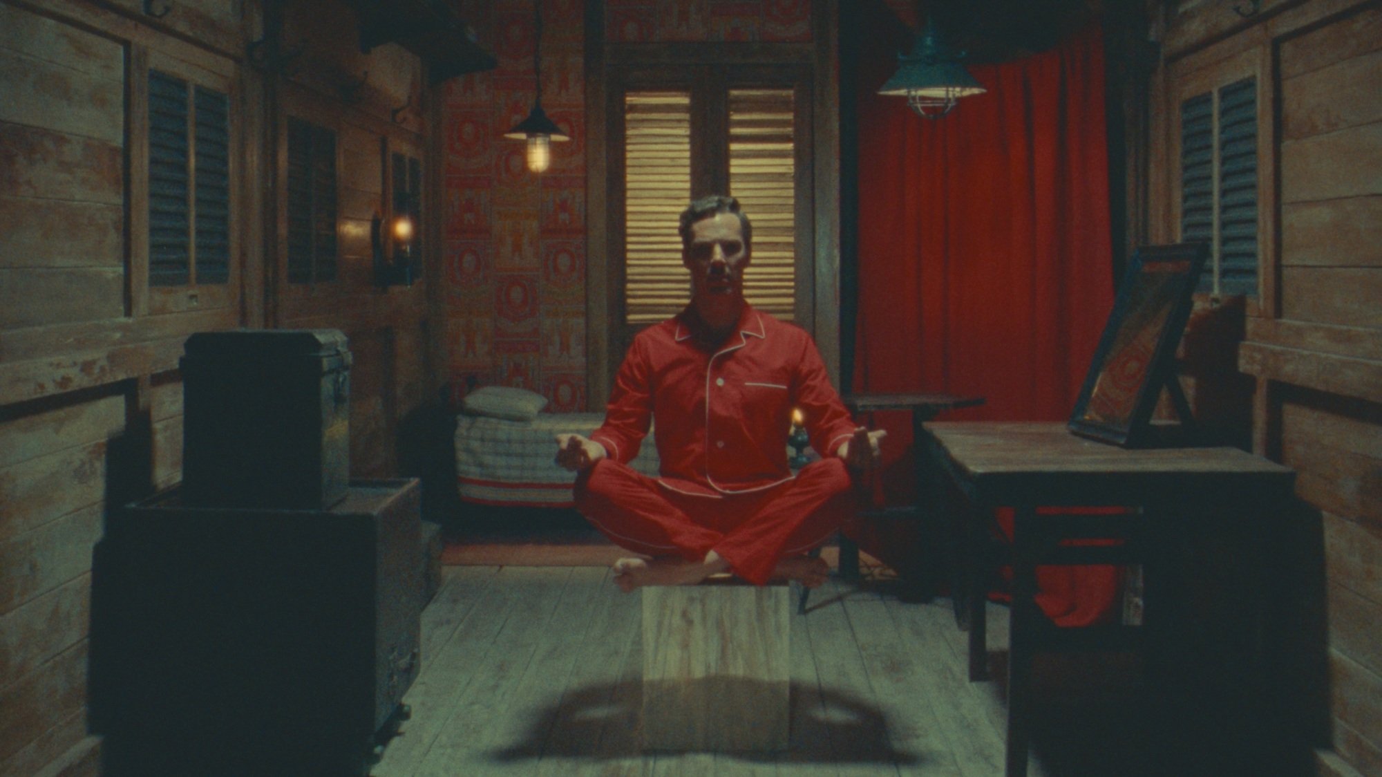 Un homme en pyjama rouge lévite du sol dans une petite pièce.