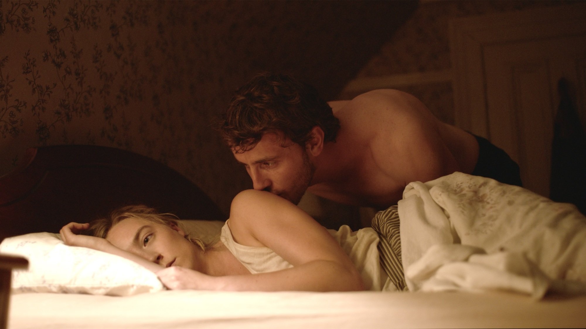 Une femme est allongée sur son lit et un homme lui embrasse l'épaule.