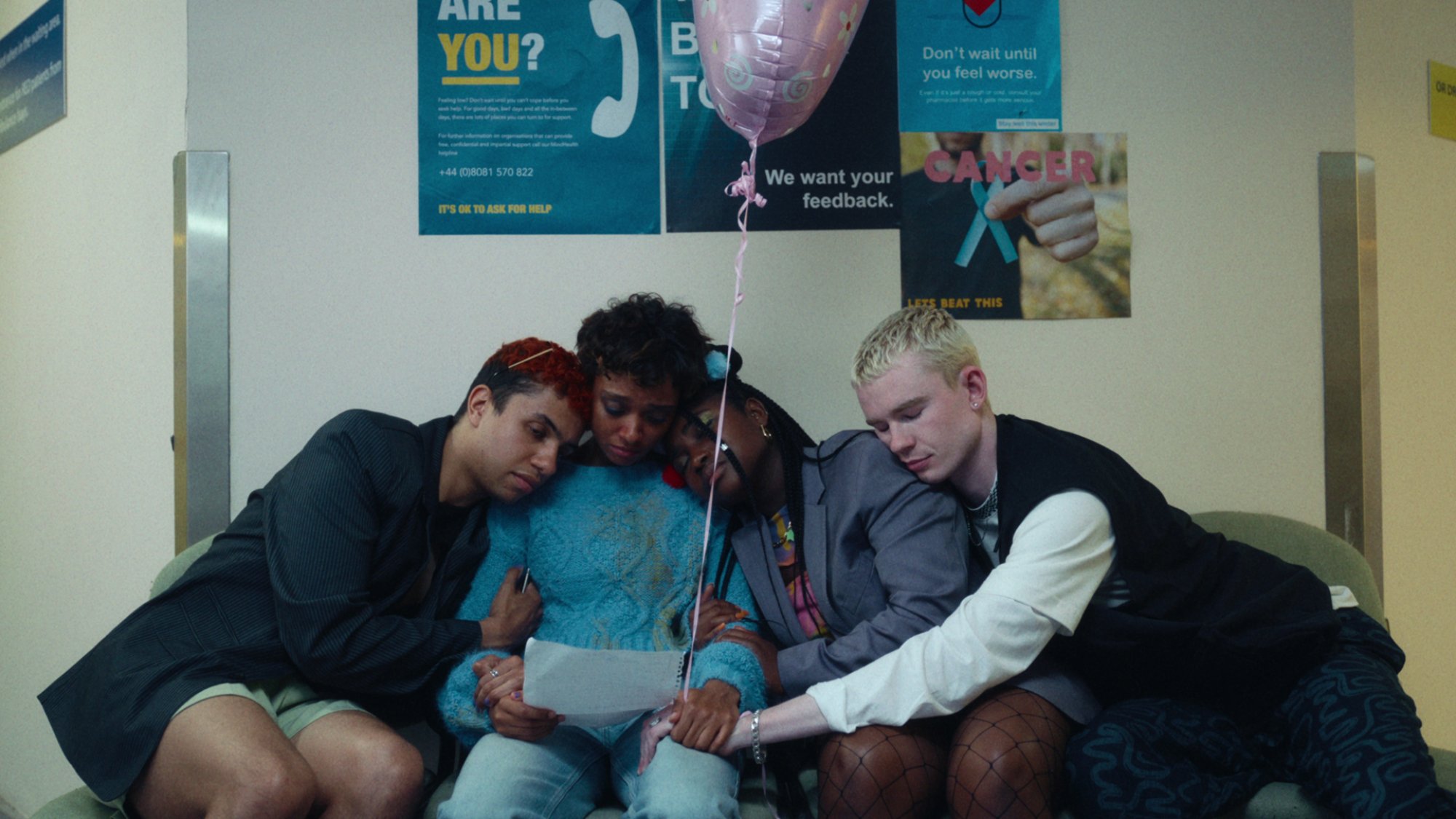 Quatre adolescents s'embrassent en tenant un morceau de papier et un ballon.